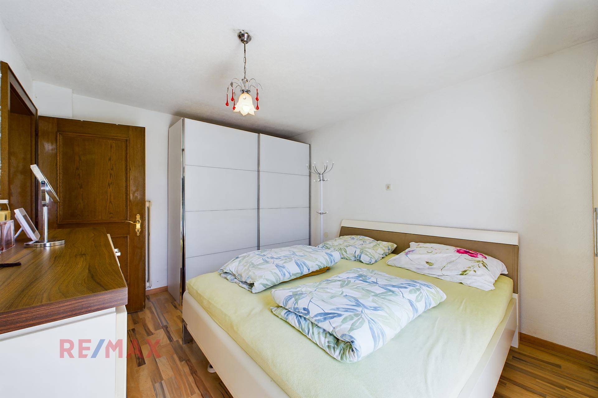 Schlafzimmer mit hellem Parkettboden, großem Kleiderschrank und einem Fenster für Tageslicht.