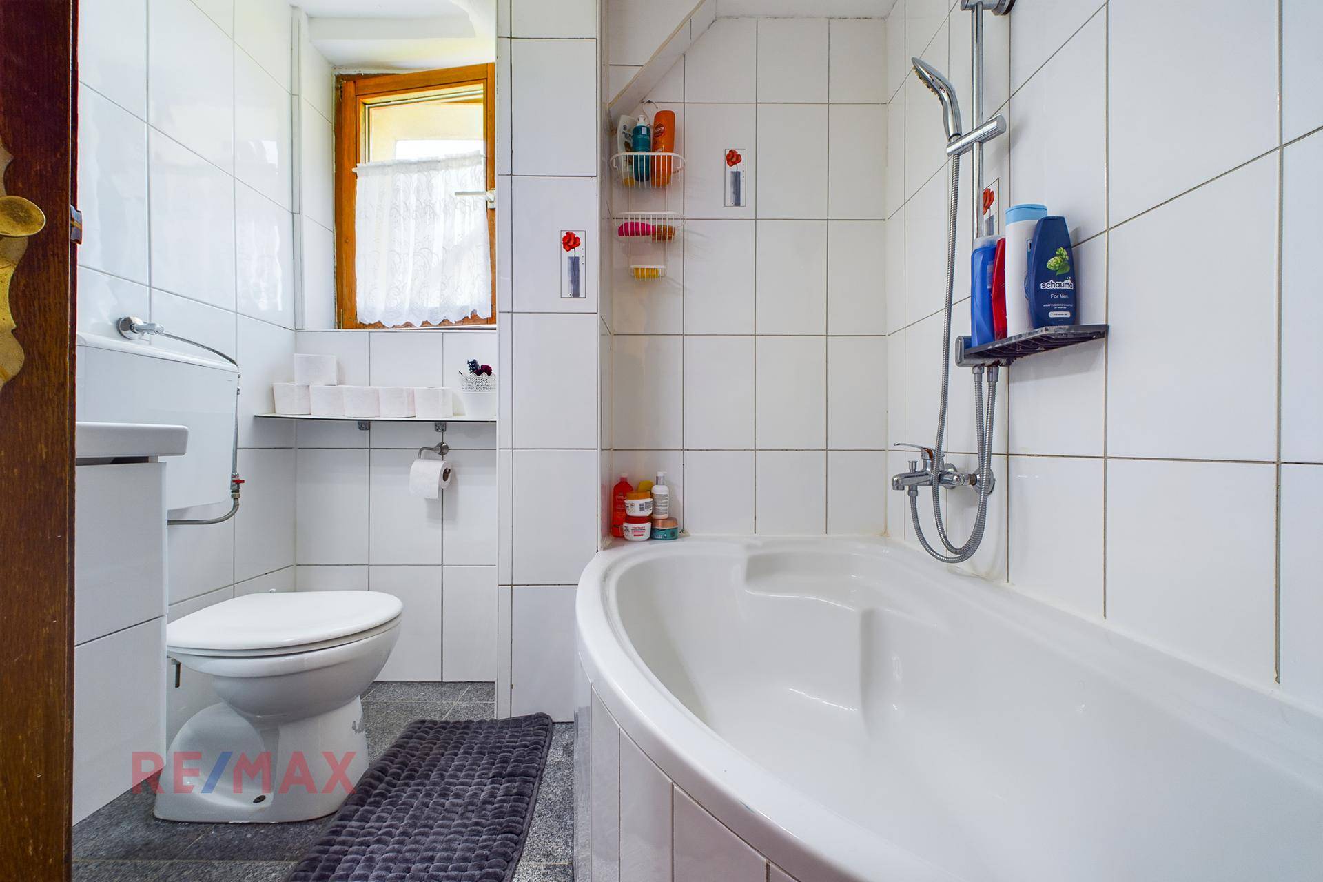 Badezimmer mit Badewanne, WC und weißen Fliesen an Wänden und Boden.