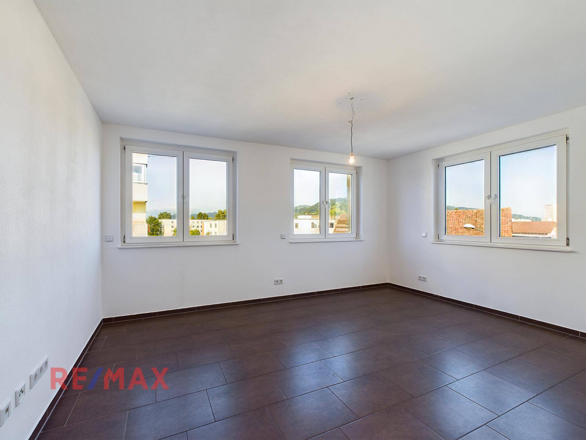 Helles Zimmer mit drei Fenstern und Fliesenboden, ideal als Wohn- oder Schlafzimmer.
