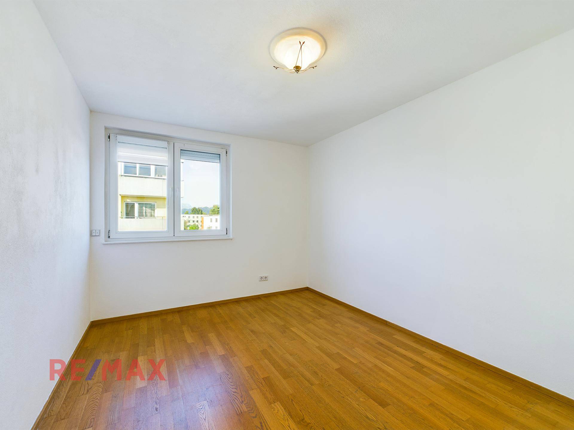 Schlafzimmer mit hellem Parkettboden und Fenster für natürliche Belichtung.