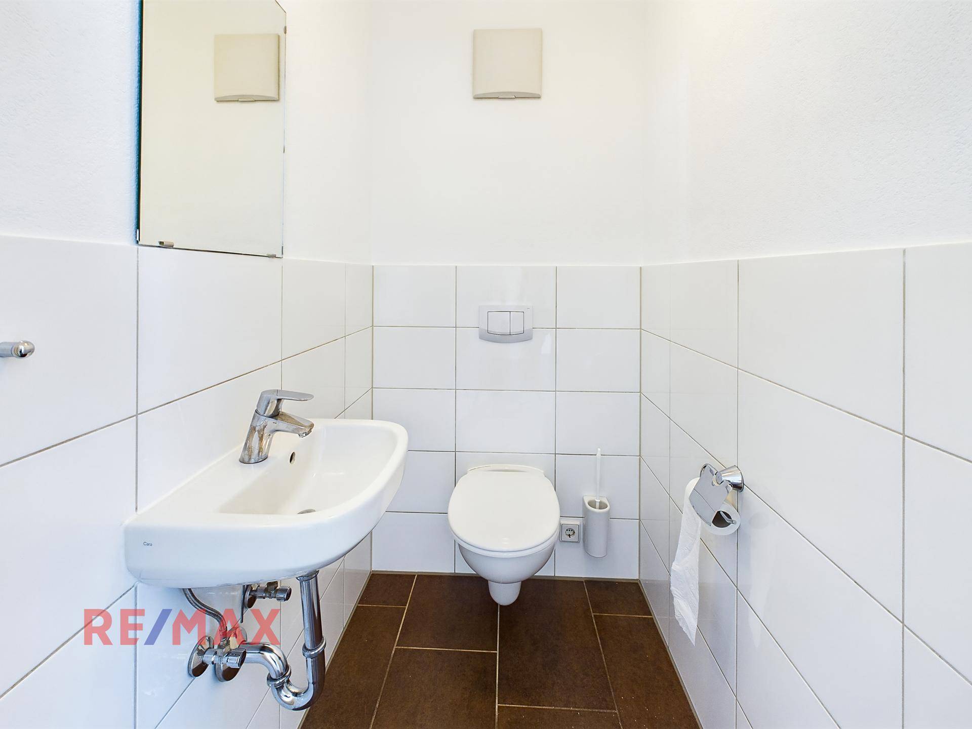 Modern gefliestes Gäste-WC mit wandhängendem WC und Waschbecken.