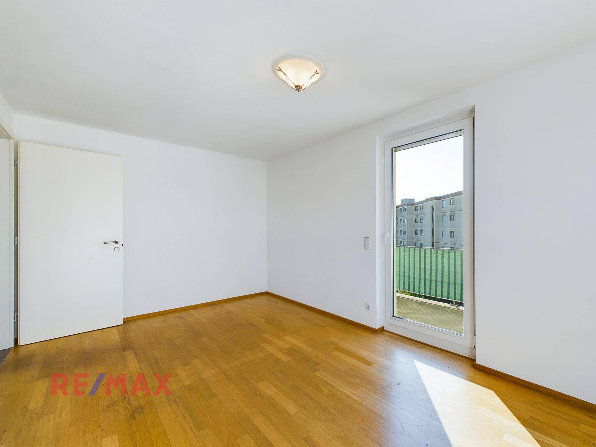 Schlafzimmer mit Parkettboden und Balkonzugang, gut belichtet.