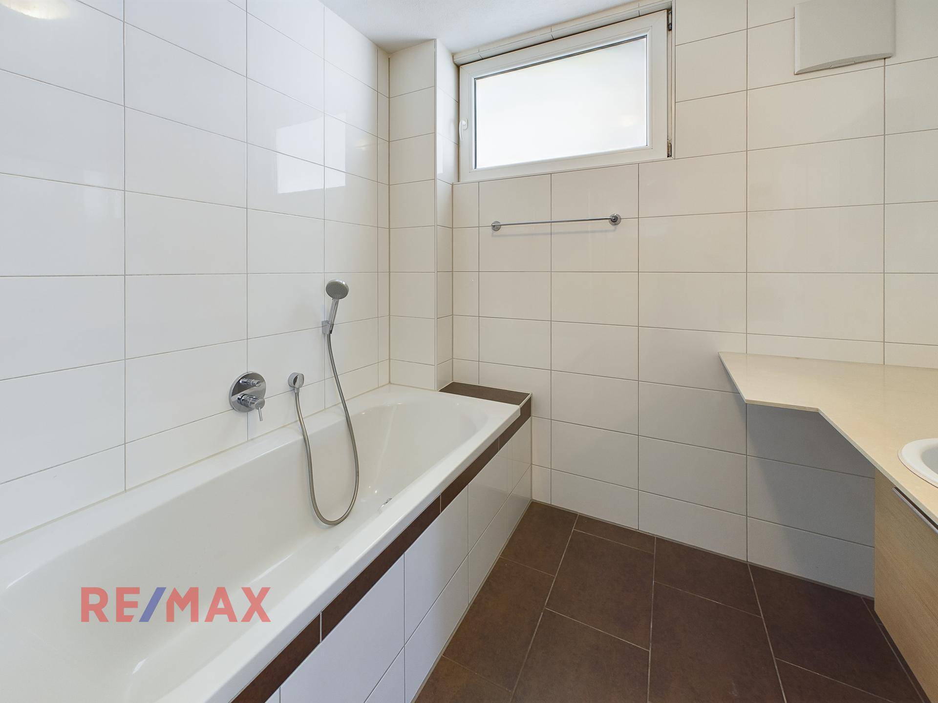 Badezimmer mit Badewanne und Fenster, hell gefliest.