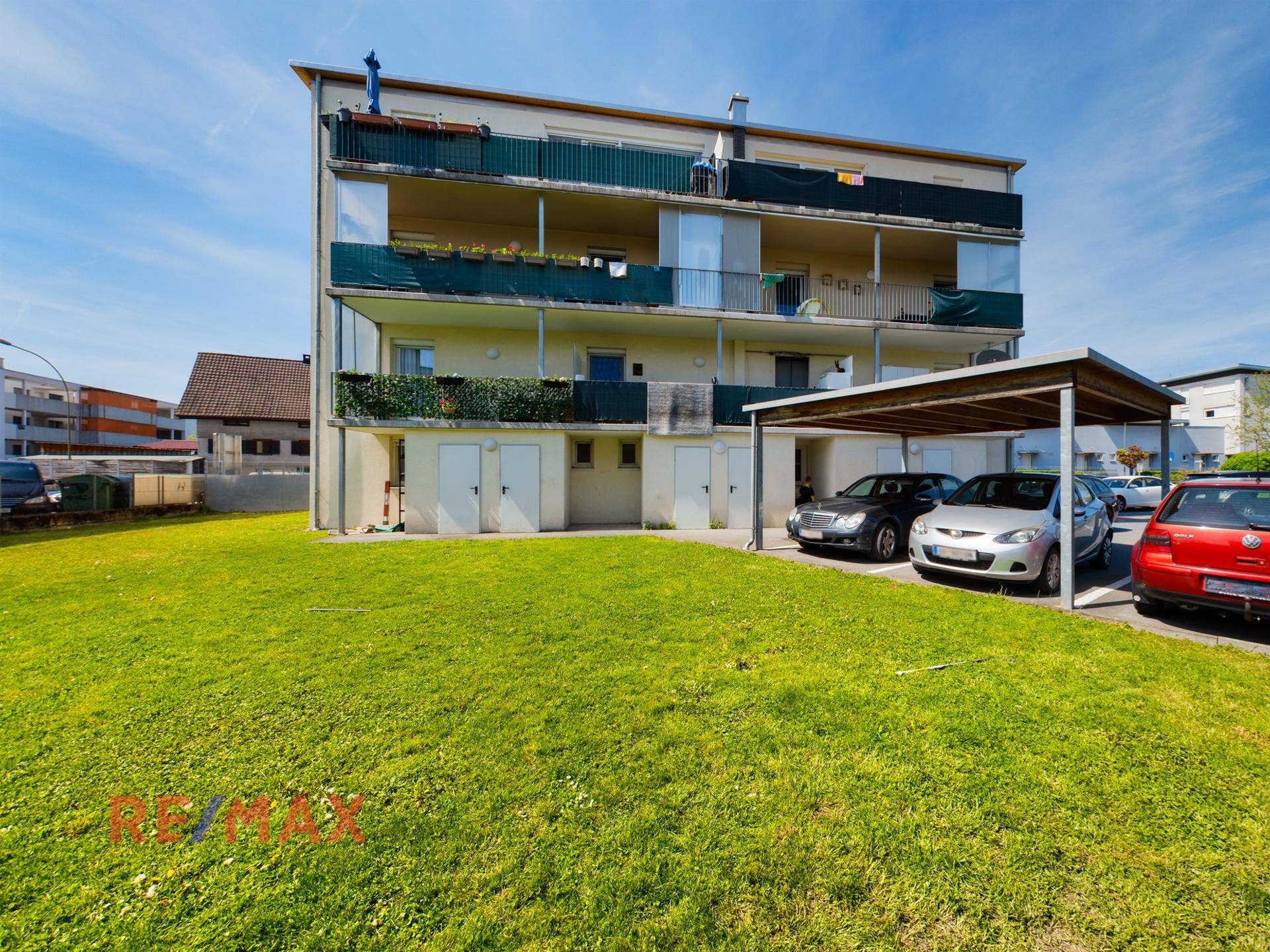 Mehrfamilienhaus mit Grünfläche, Balkonen und Carport-Parkplätzen.