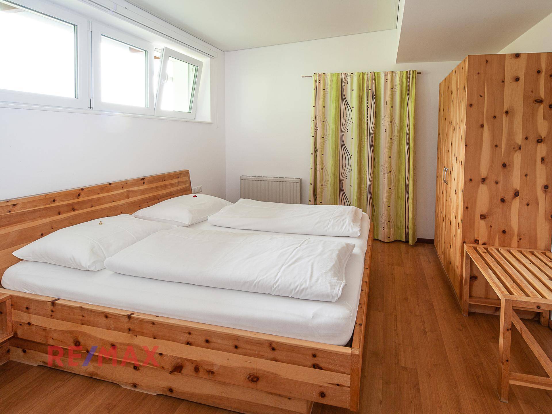 Schlafzimmer mit hellem Holzbett, passendem Kleiderschrank und Holzboden, gut beleuchtet durch Fenster.