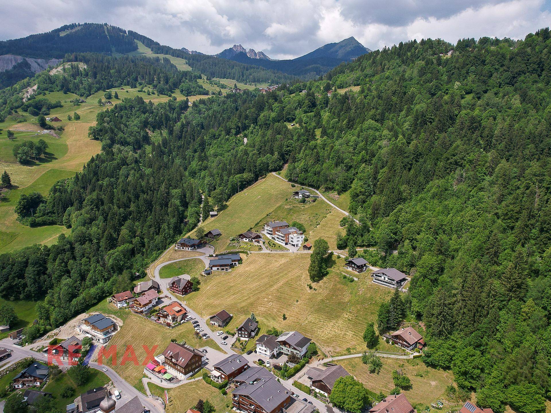Panoramablick aus der Vogelperspektive auf die ländliche Siedlung, umgeben von dichten Wäldern und Bergen.