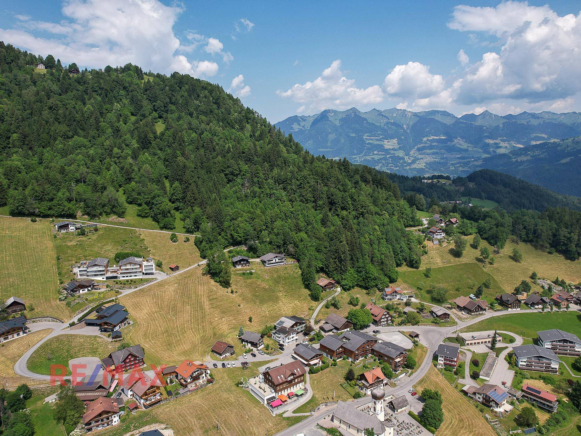 Weitläufige Luftaufnahme der ländlichen Umgebung mit bewaldeten Hügeln und Berggipfeln in der Ferne.