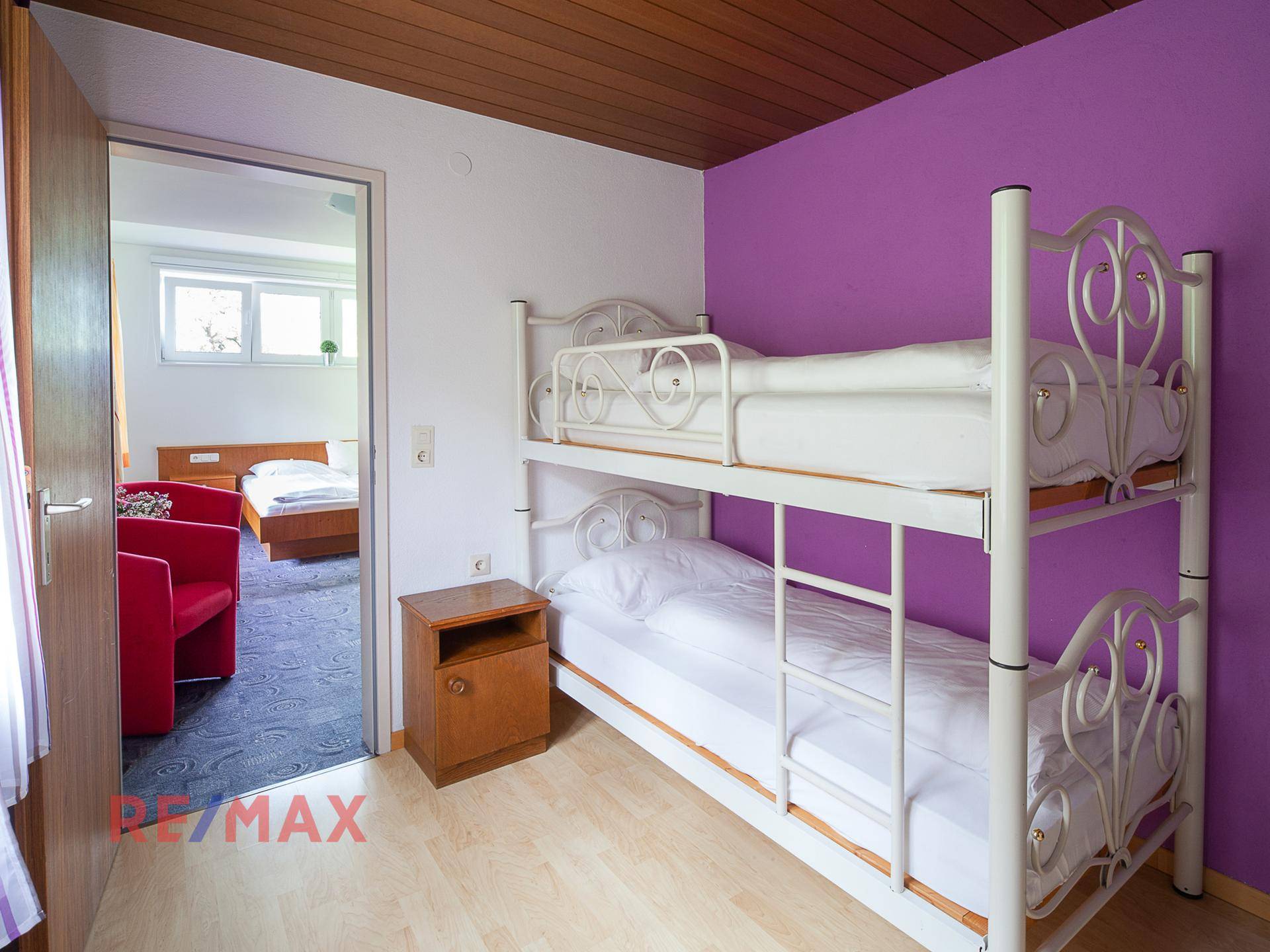 Kinderzimmer mit Etagenbett und lila Wand, angrenzend an ein weiteres Schlafzimmer.