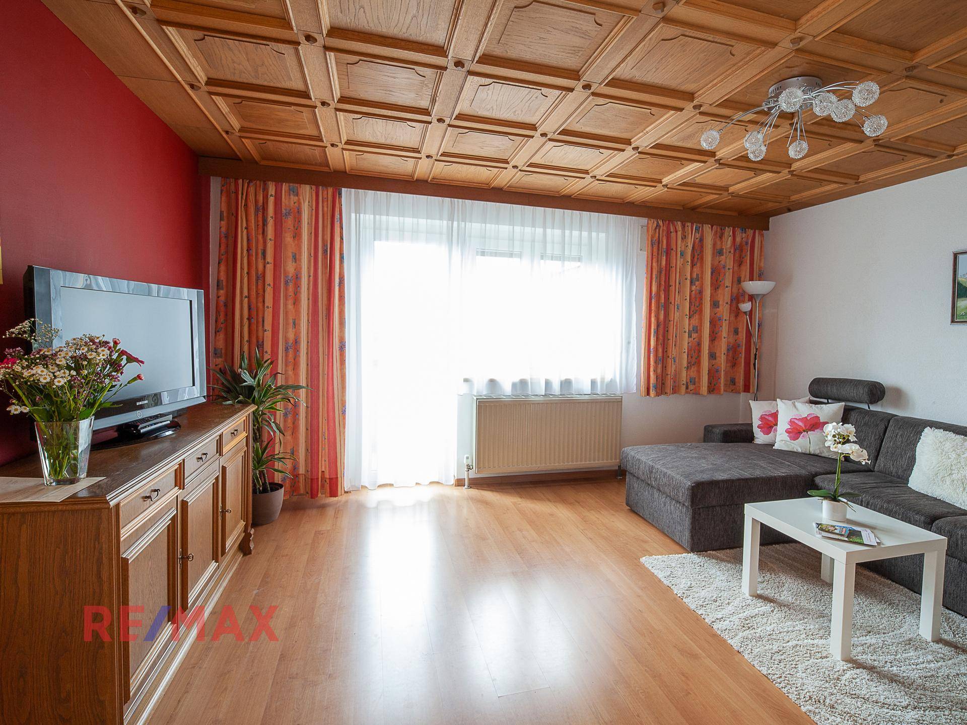Helles Wohnzimmer mit großem Fenster, Sofa, TV-Möbel und Holzkassettendecke.