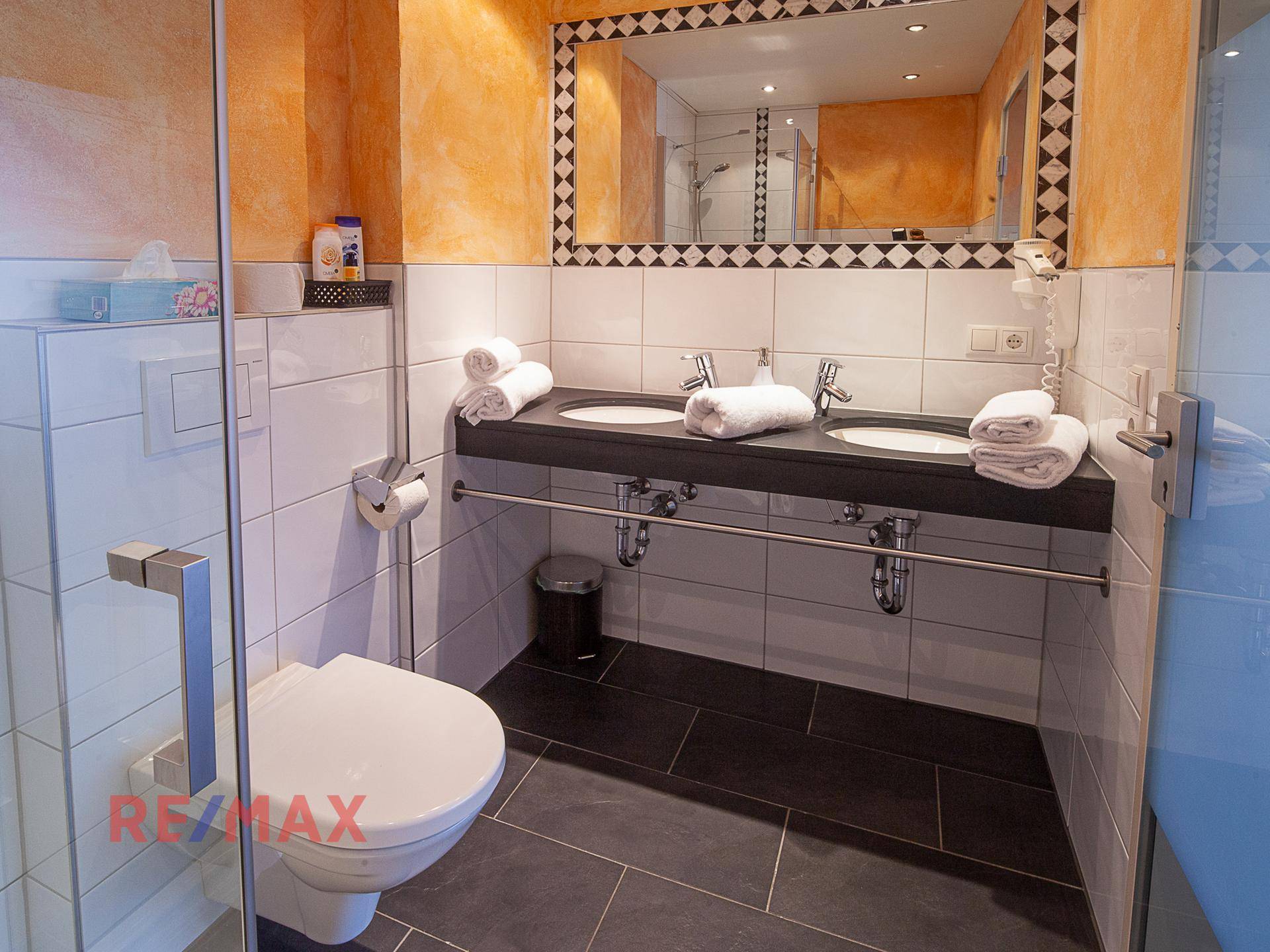 Badezimmer mit Doppelwaschbecken, wandhängendem WC und Duschbereich, gefliest in Schwarz und Weiß.