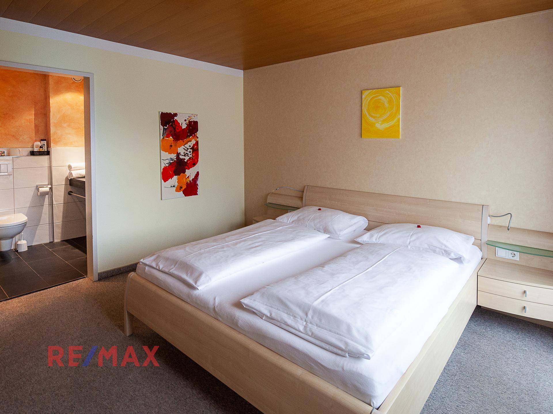 Schlafzimmer mit Doppelbett, Teppichboden und Zugang zu einem angrenzenden Badezimmer.