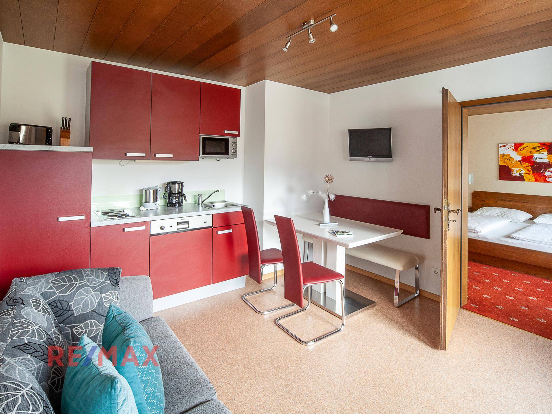 Kompakter Wohnbereich mit roter Küchenzeile, Esstisch und Sofa, ideal für kleine Apartments.