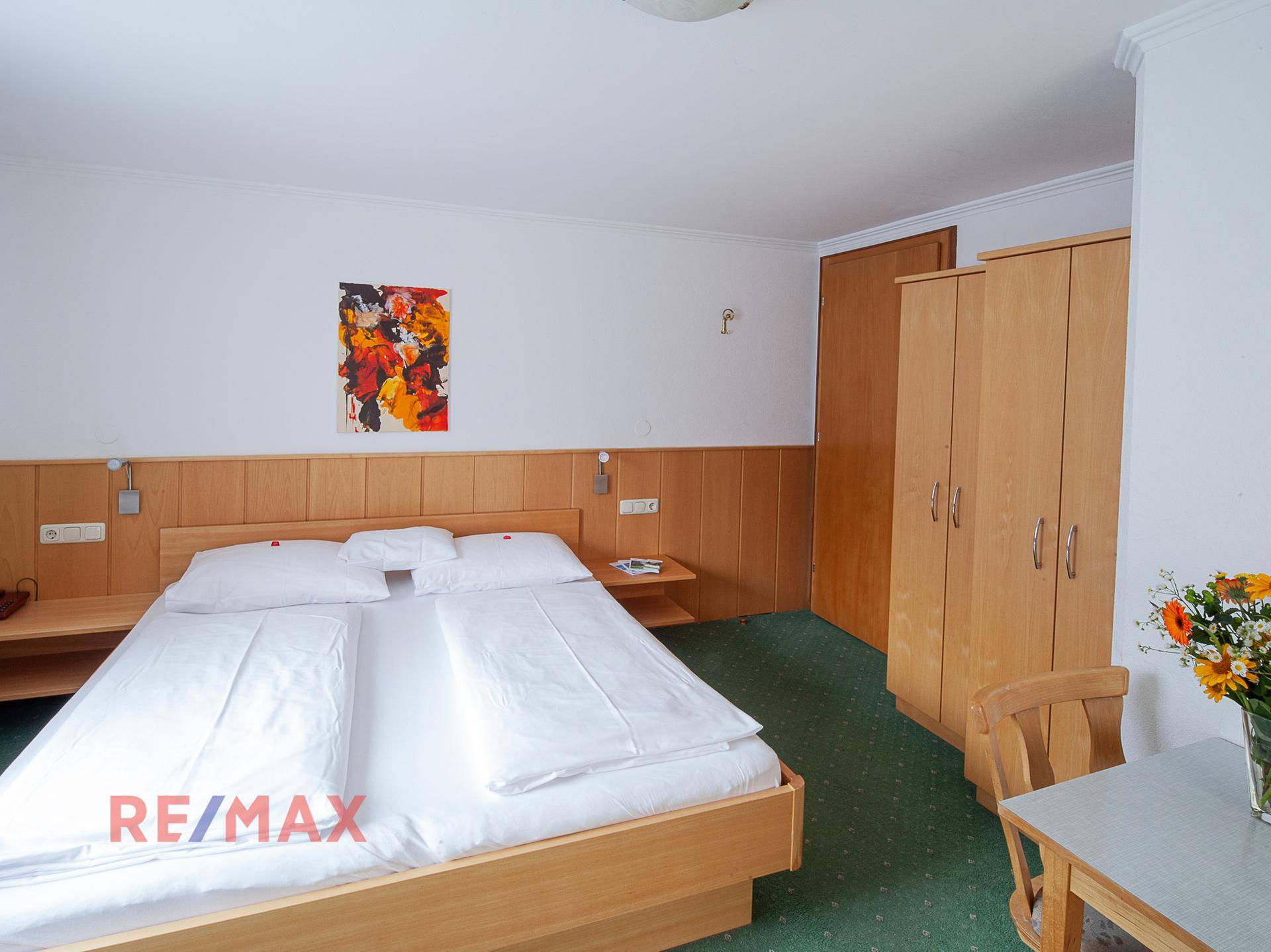 Schlafzimmer mit Doppelbett, Holzmöbeln und grünem Teppichboden, in gutem Zustand.