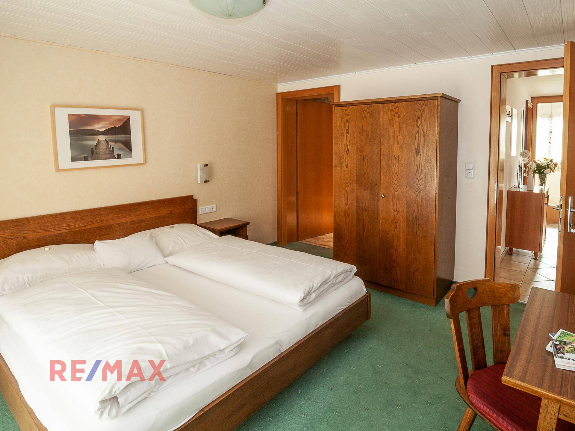 Schlafzimmer mit Doppelbett, Holzschrank und grünem Teppichboden, mit Blick auf den Flur.