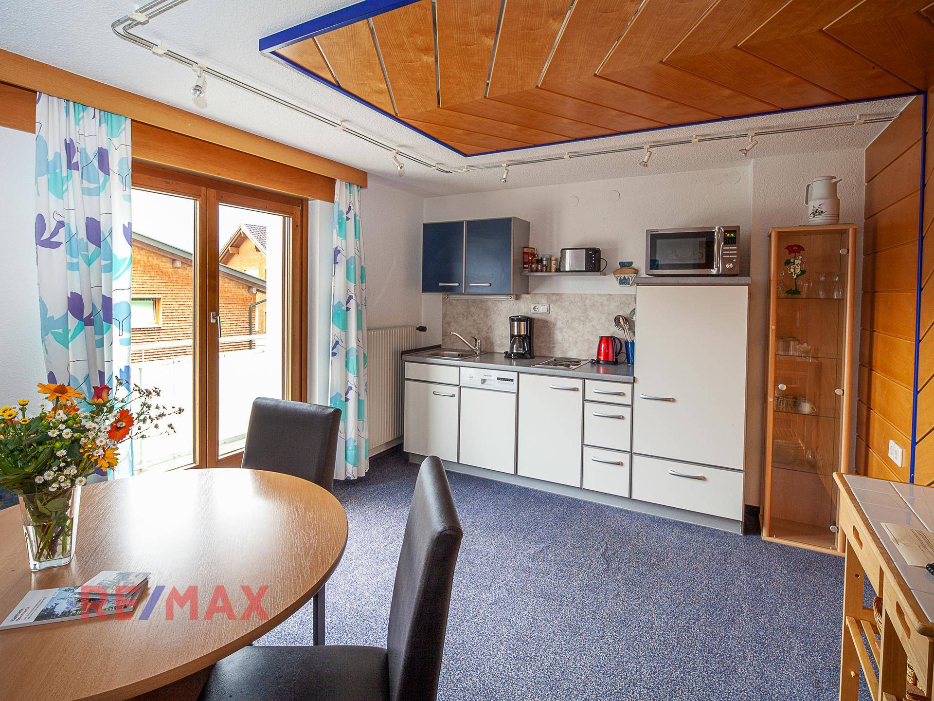 Küchen- und Essbereich mit weißer Küchenzeile, Esstisch und Zugang zu einem Balkon.