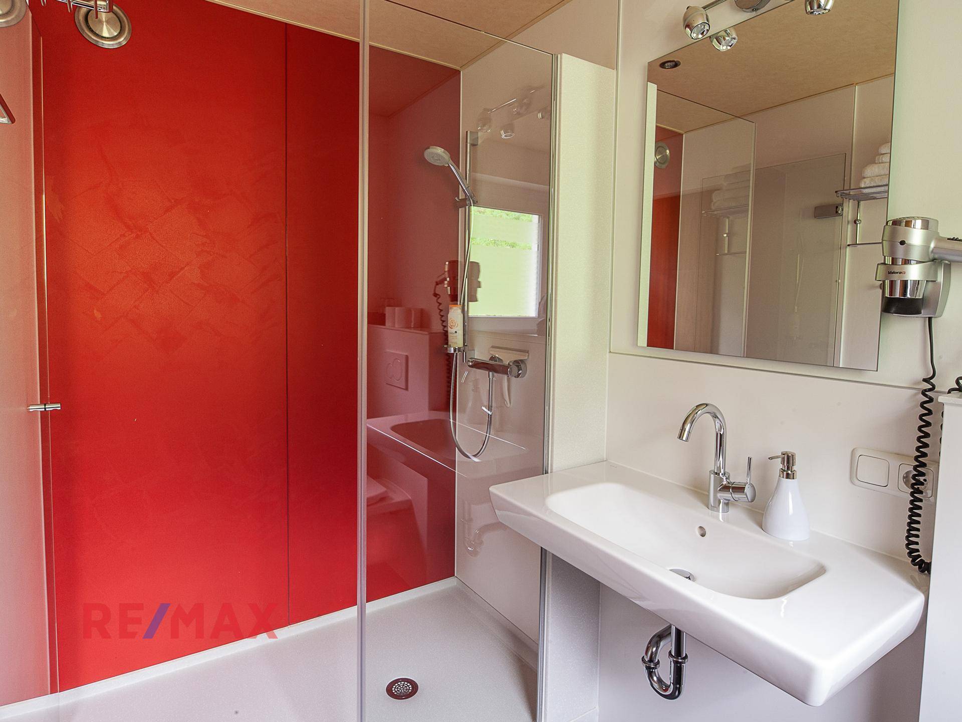 Modernes Badezimmer mit Duschkabine, Waschbecken und roter Akzentwand.