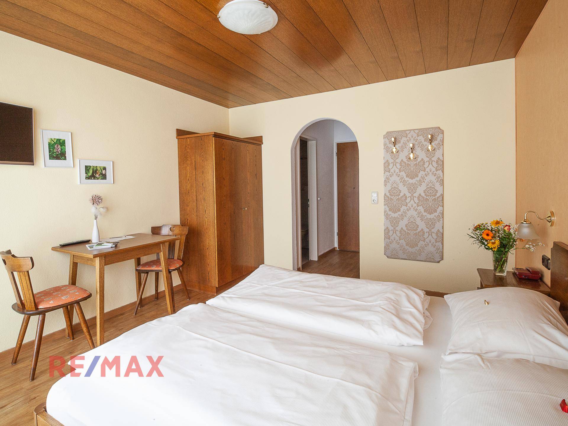 Schlafzimmer mit Doppelbett, Holzschrank und Holzboden, mit traditioneller Deckenverkleidung.