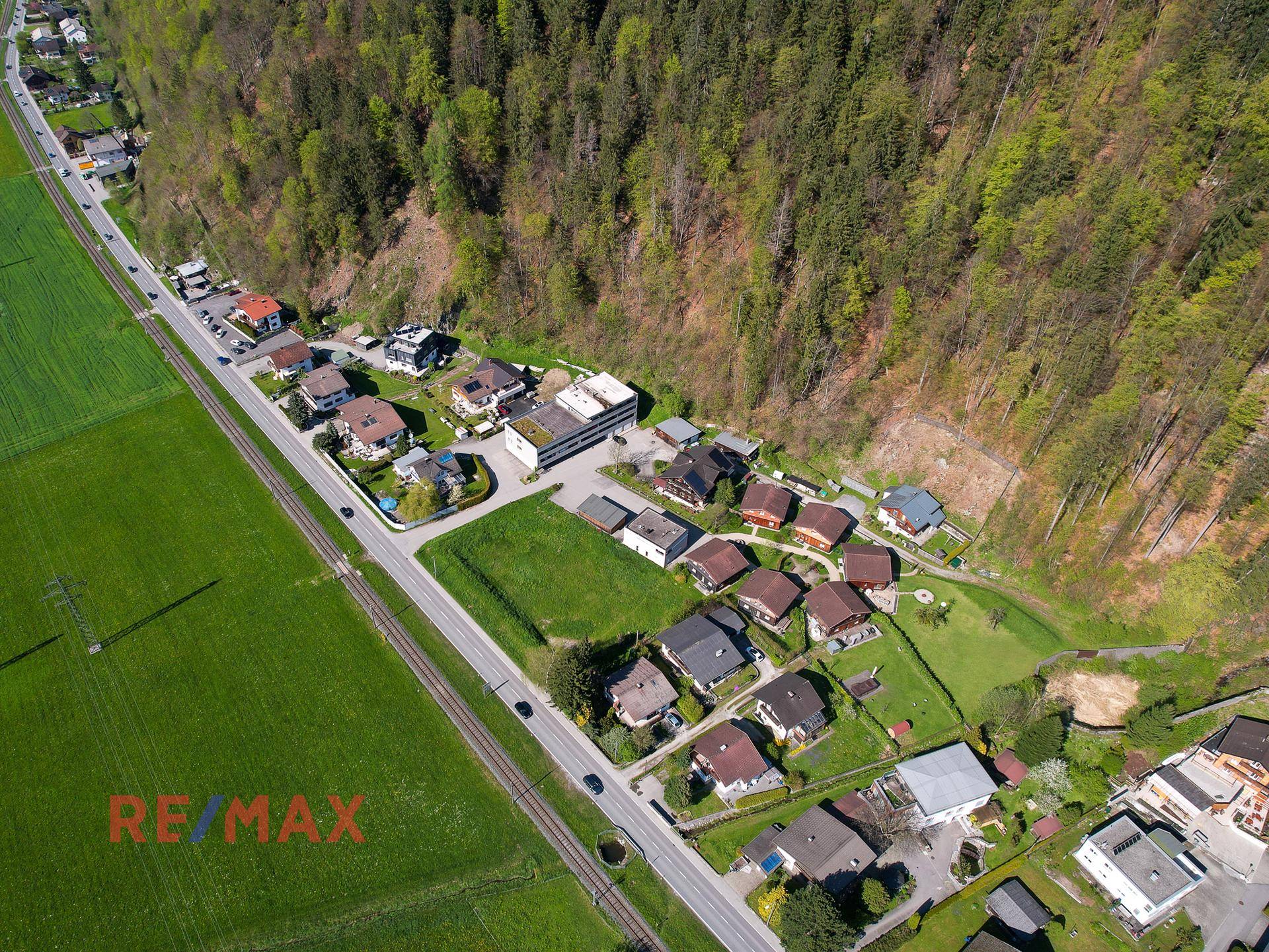 Detaillierte Luftaufnahme des Grundstücks mit angrenzender Straße, Wohnhäusern und bewaldetem Hang.