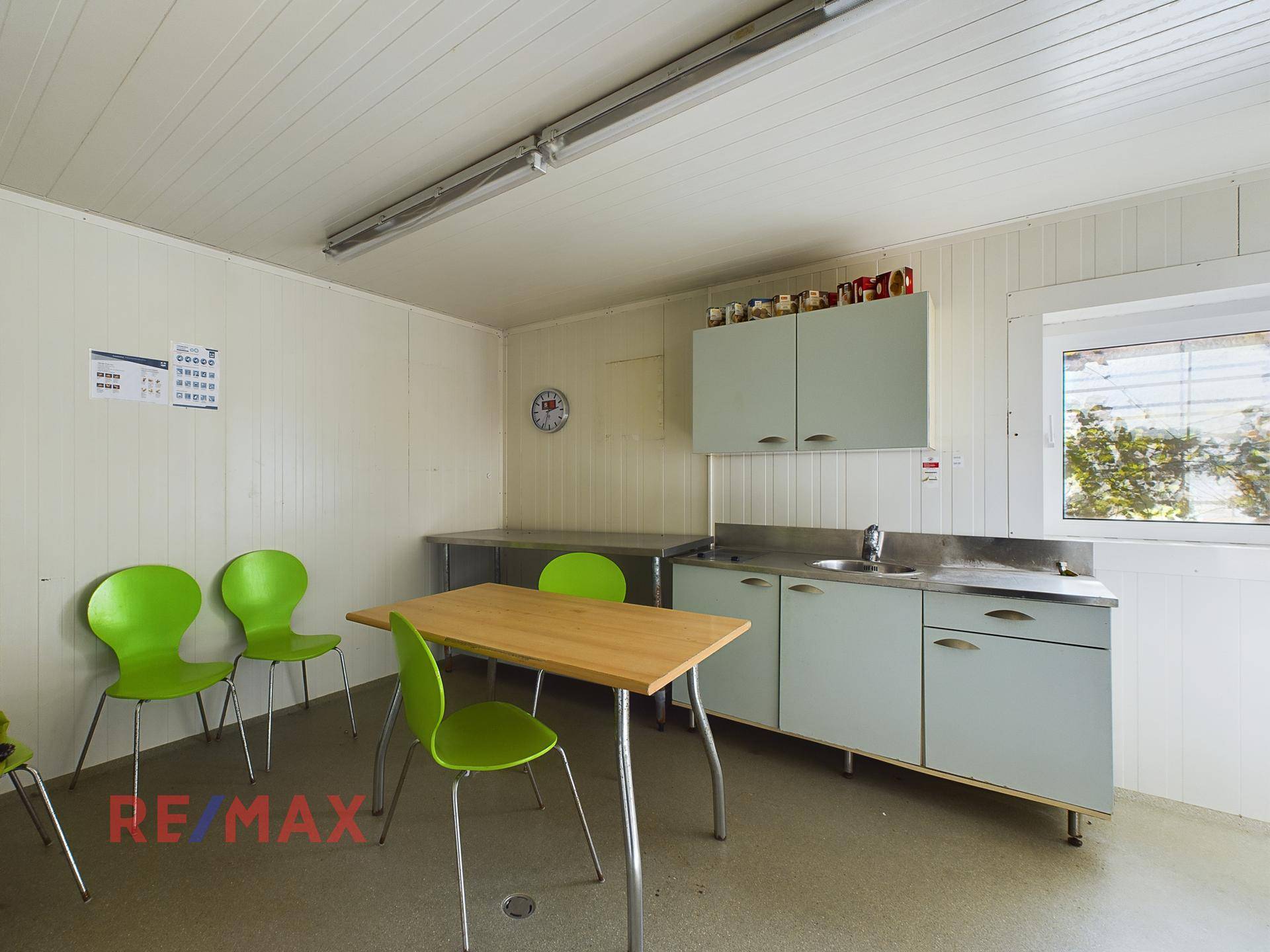 Einfacher Pausenraum mit kleiner Küchenzeile, Tisch und grünen Stühlen, ideal für Mitarbeiter.