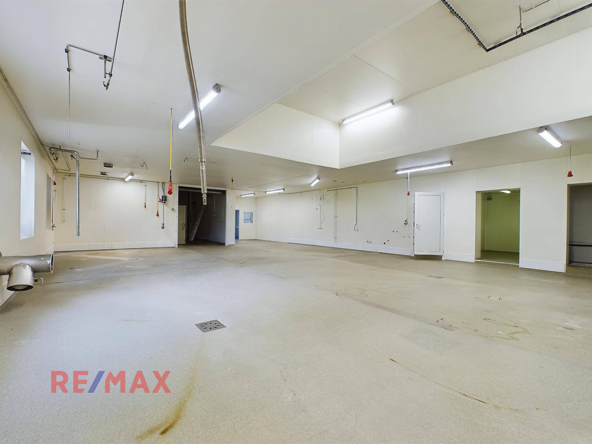Großer, leerer Industrieraum mit sichtbaren Installationen an den Wänden und Betonboden.