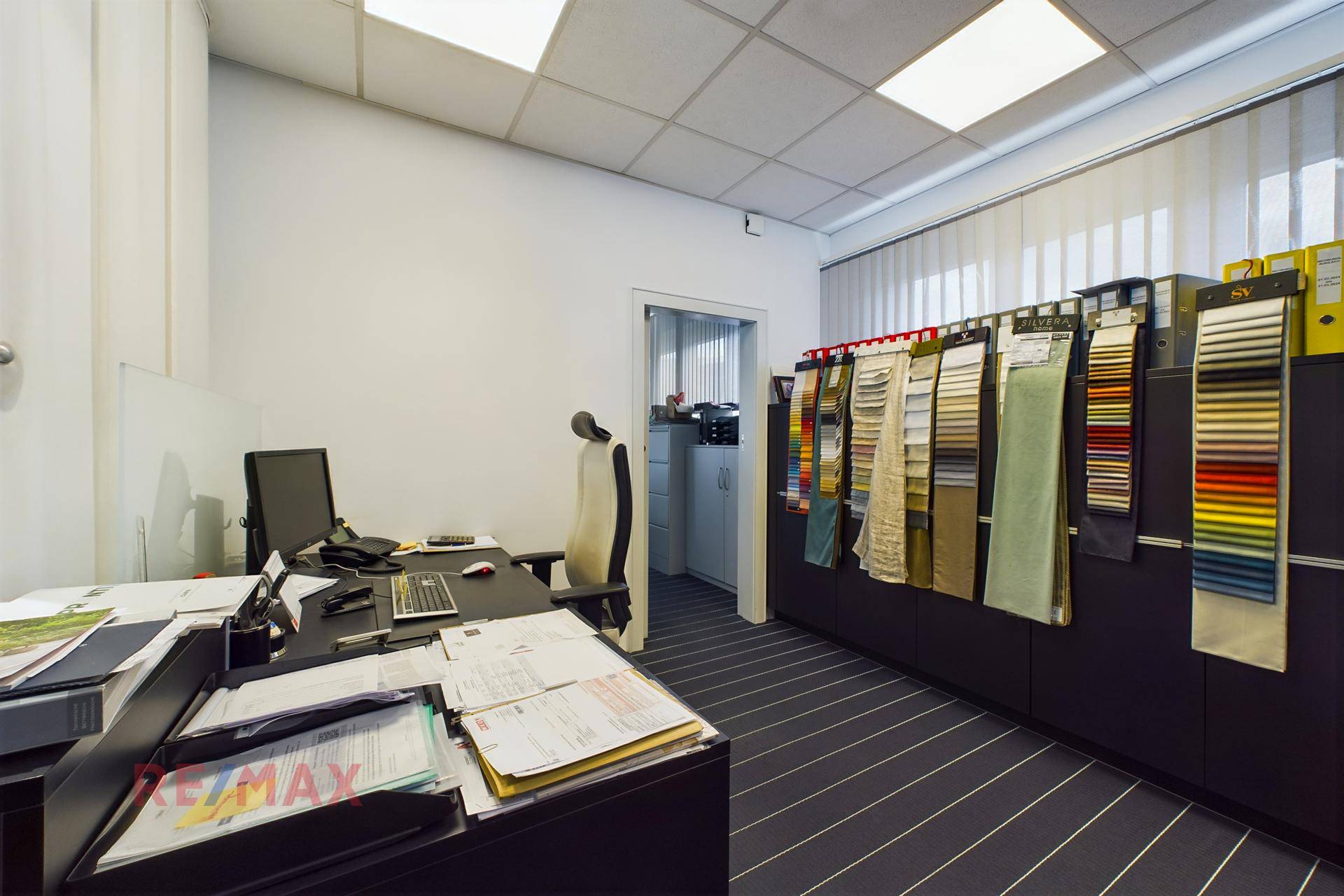 Funktionales Büro mit Schreibtisch, Bürostuhl und Regalen voller Stoffmuster und Akten.