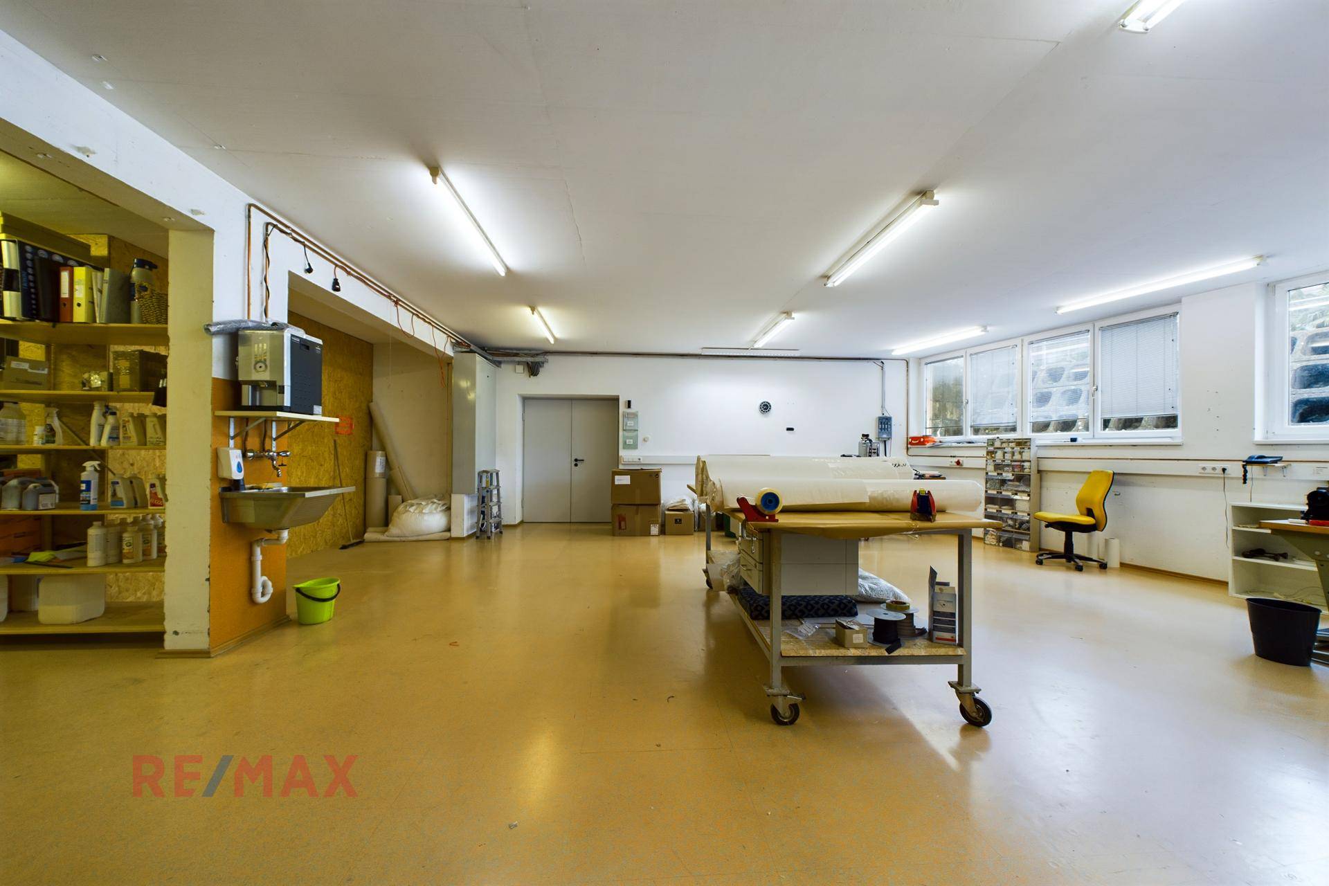 Geräumiger Werkstattbereich mit großen Fenstern, Arbeitstischen und einem Waschbecken.