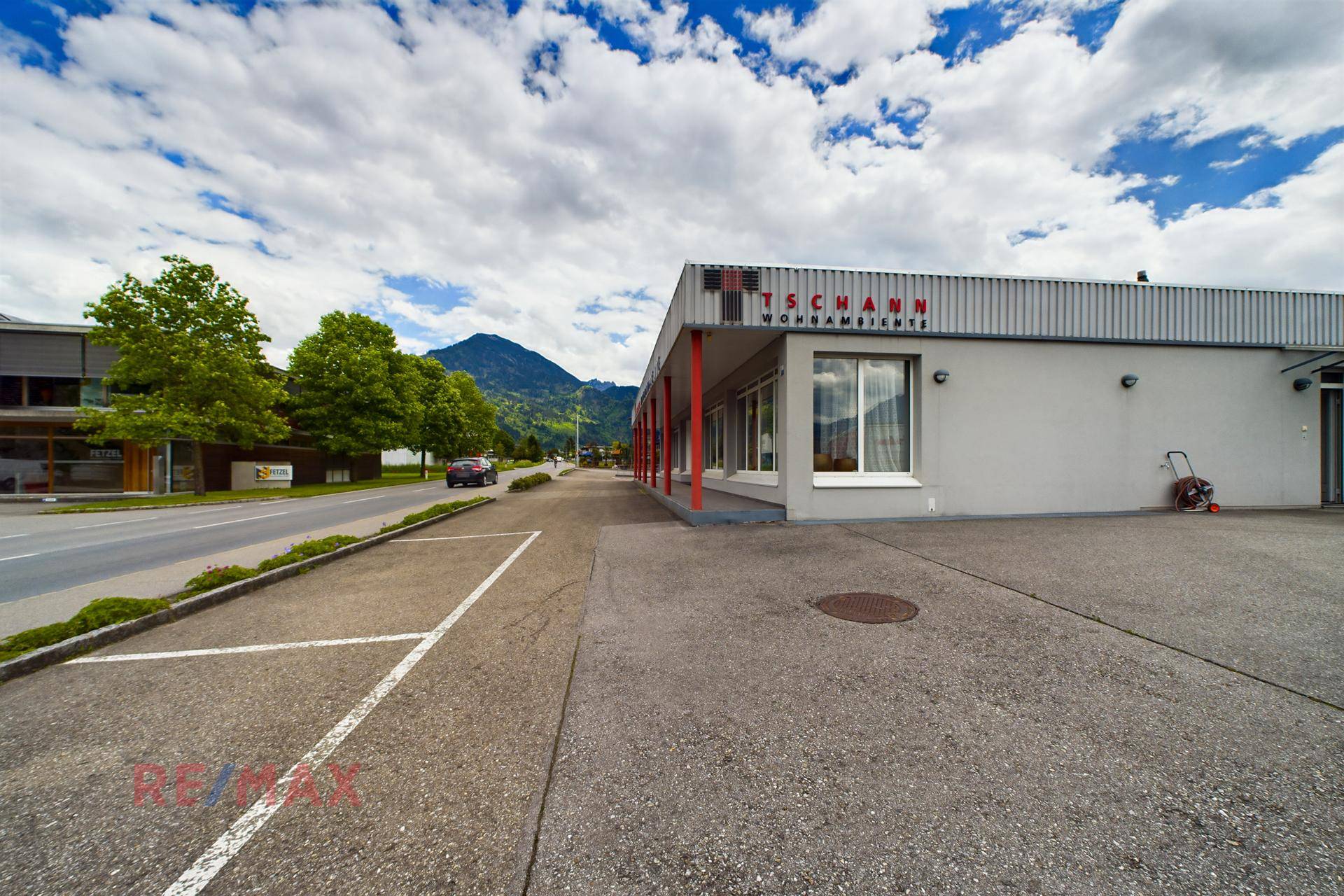 Ansicht des Geschäftsgebäudes mit Parkplätzen, umgeben von Bäumen und Bergen im Hintergrund.