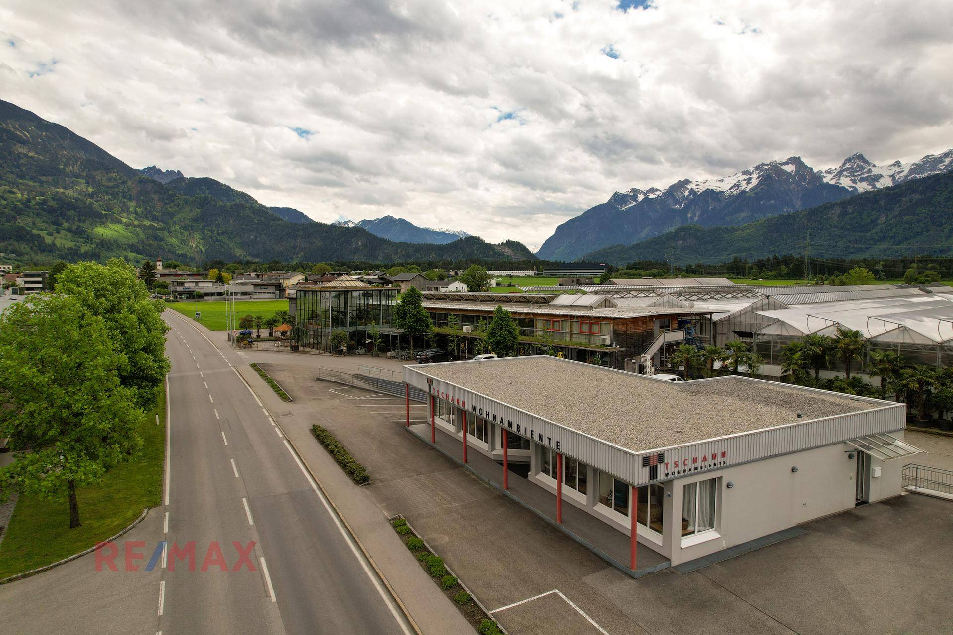 Luftaufnahme des Gewerbegebiets mit dem Hauptgebäude, umliegenden Feldern und Bergpanorama.
