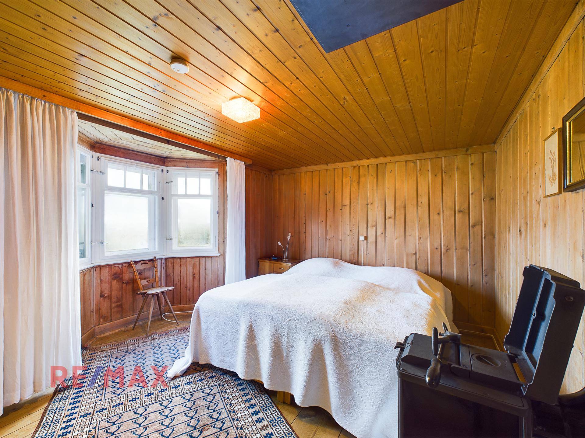 Gemütliches Schlafzimmer mit Holztäfelung, Holzboden und Erkerfenster.