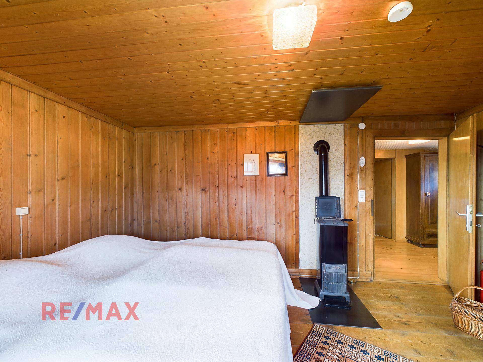 Schlafzimmer mit Holztäfelung, Holzboden und einem Holzofen für zusätzliche Wärme.