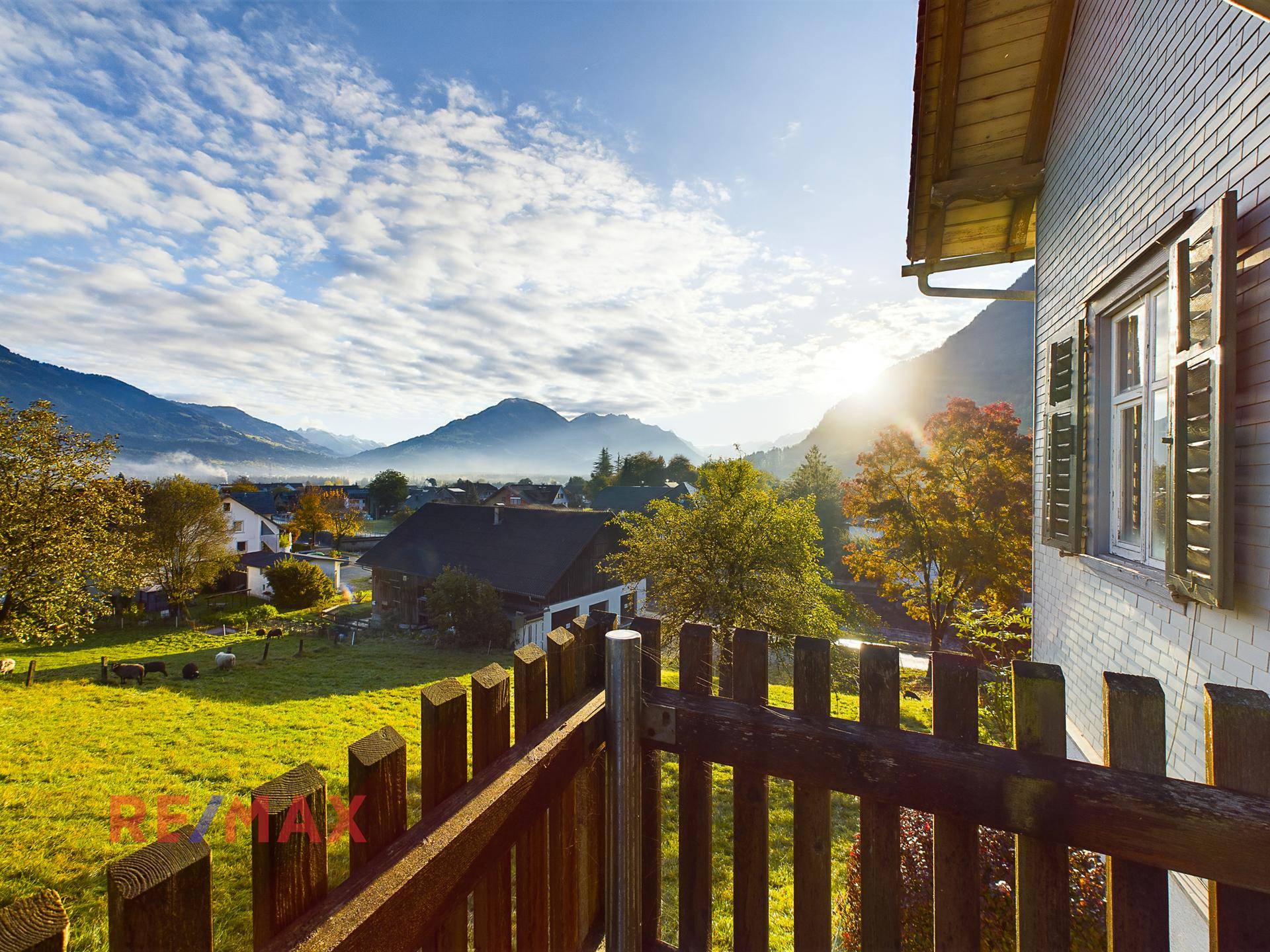 Blick von einem Balkon auf grüne Wiesen, Berge und die ländliche Umgebung.