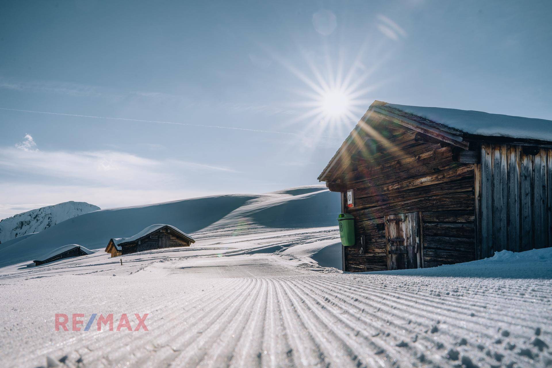 Verschneite Winterlandschaft mit einer rustikalen Holzhütte und präparierten Skipisten.