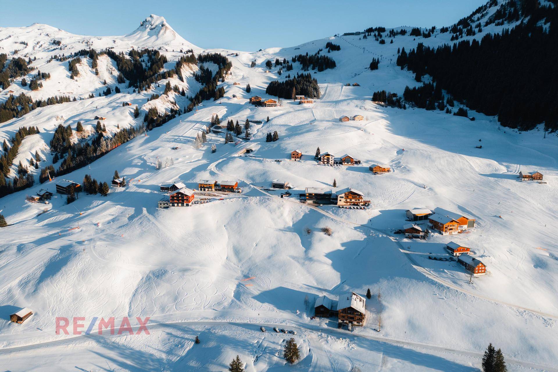 Luftaufnahme eines verschneiten Dorfes in einer malerischen Berglandschaft im Winter.
