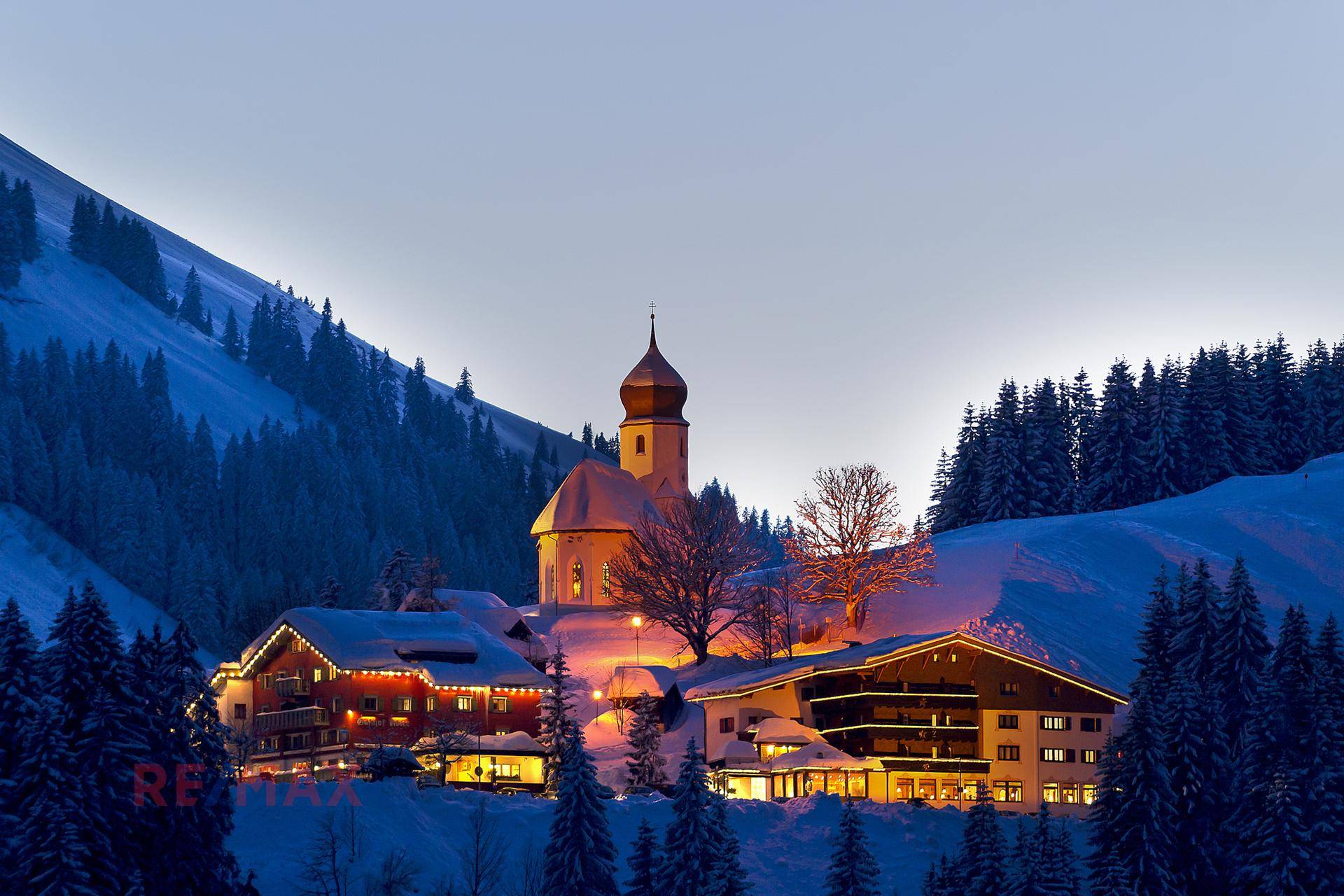 Idyllisches Bergdorf bei Dämmerung im Winter, beleuchtet mit einer Kirche im Zentrum.