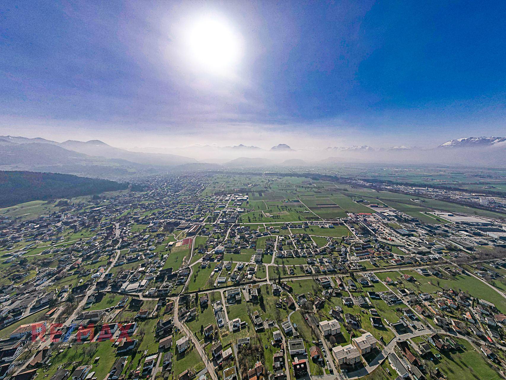 Weitläufige Luftaufnahme einer ländlichen Region mit einer Stadt, Feldern und Bergen am Horizont.