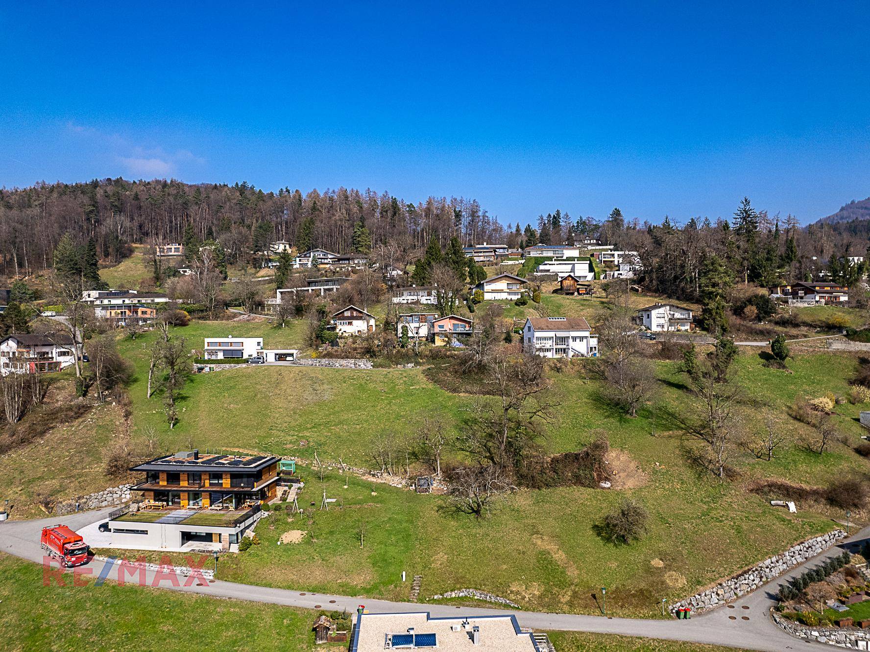Panoramablick auf ein Baugrundstück in einer grünen Wohngegend mit Bergen im Hintergrund.