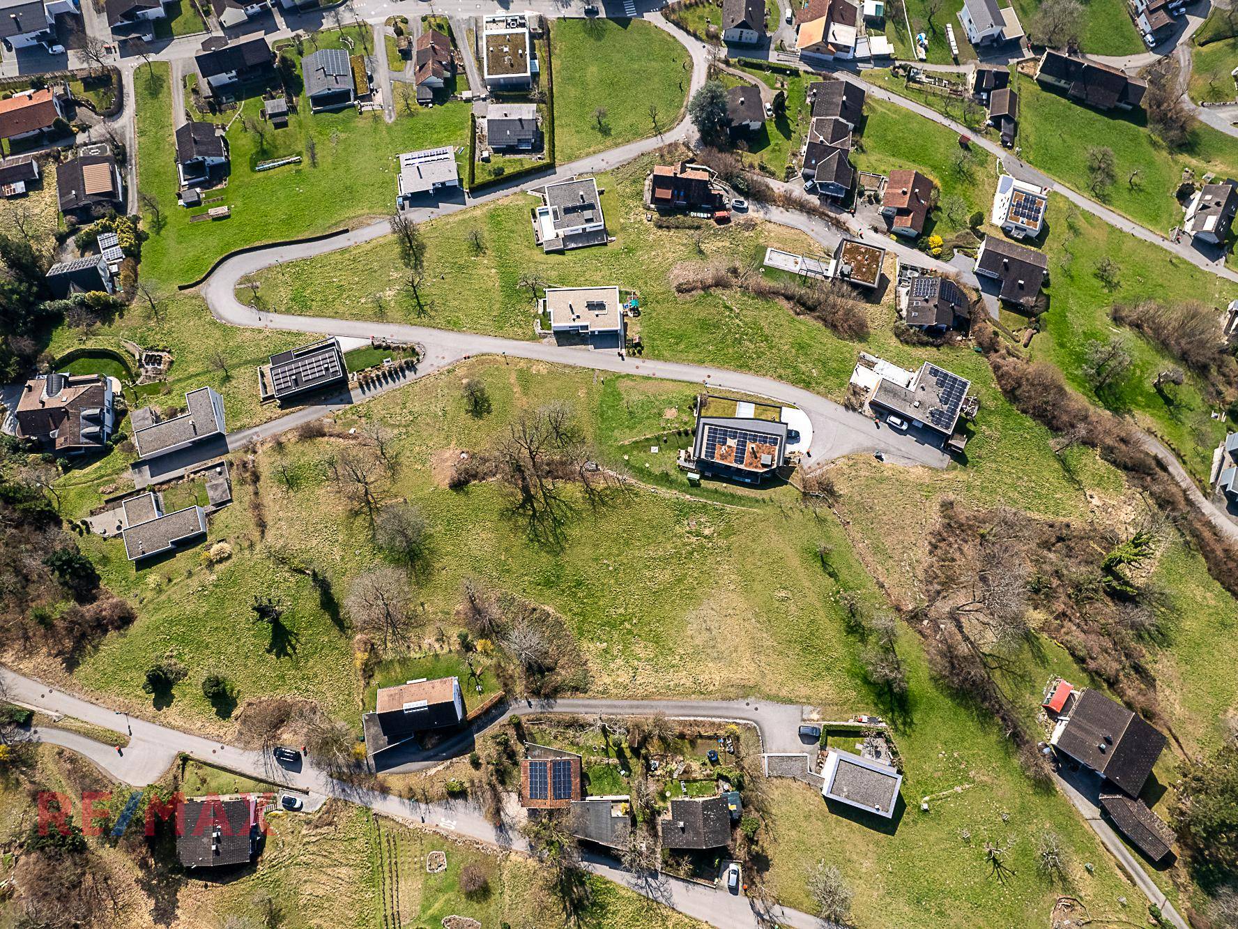 Weitläufige Luftaufnahme einer Wohnsiedlung in hügeliger Landschaft mit vielen Einfamilienhäusern.