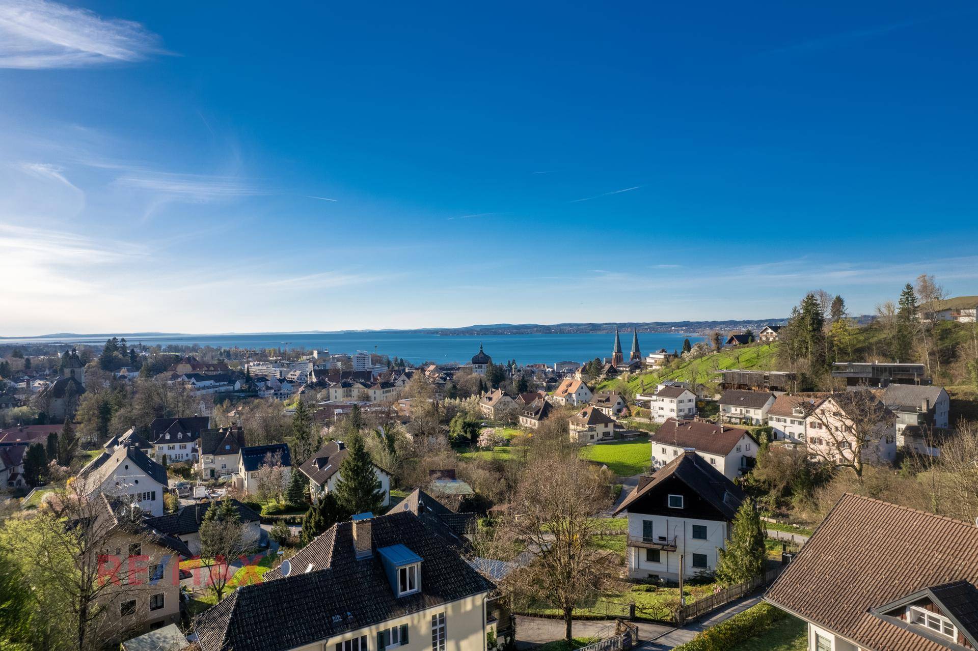 Weitläufiger Panoramablick über die Stadt und den Bodensee an einem sonnigen Tag.