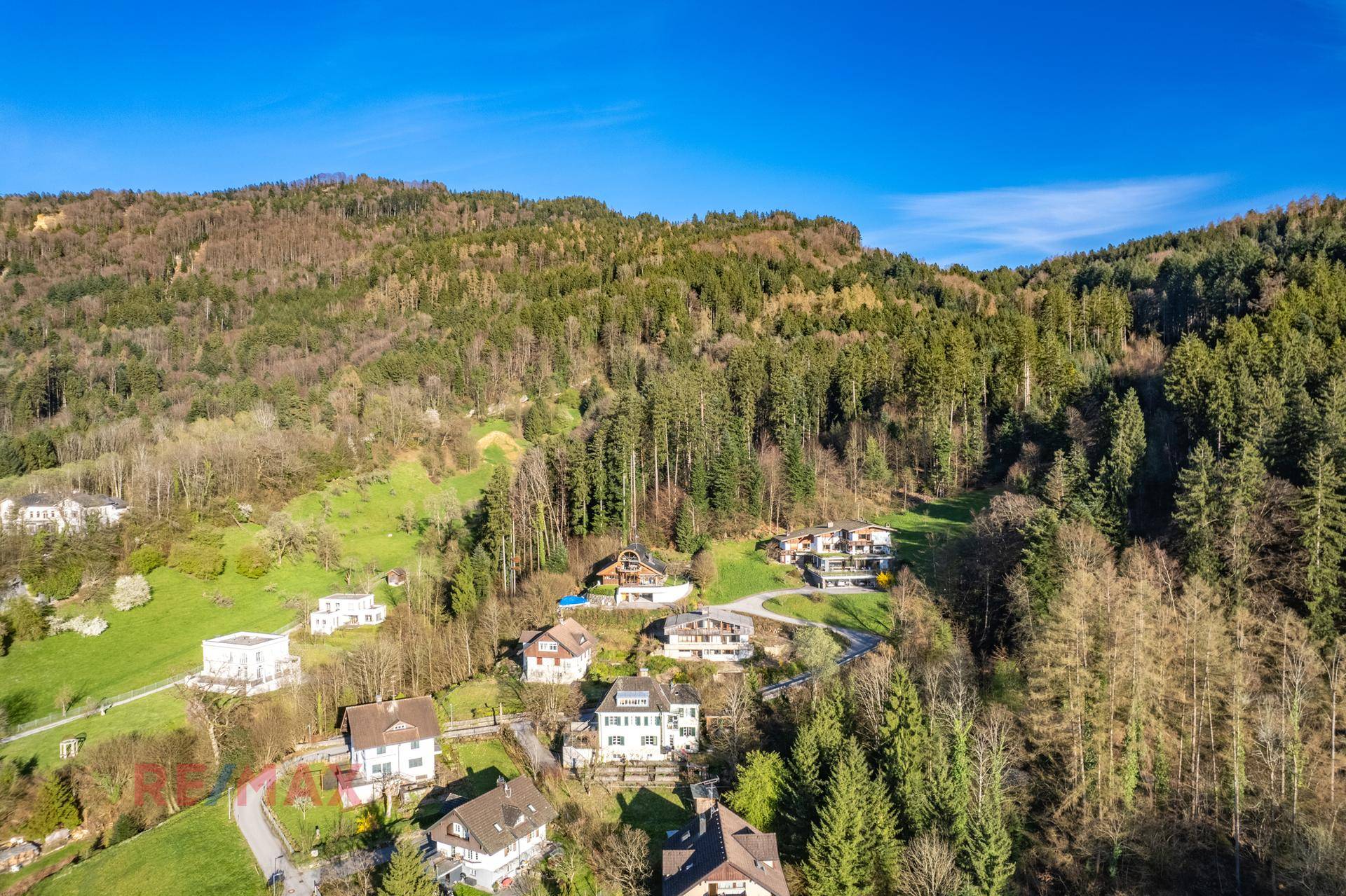 Weitwinkelaufnahme der Wohnsiedlung am bewaldeten Hang mit viel Grünfläche.