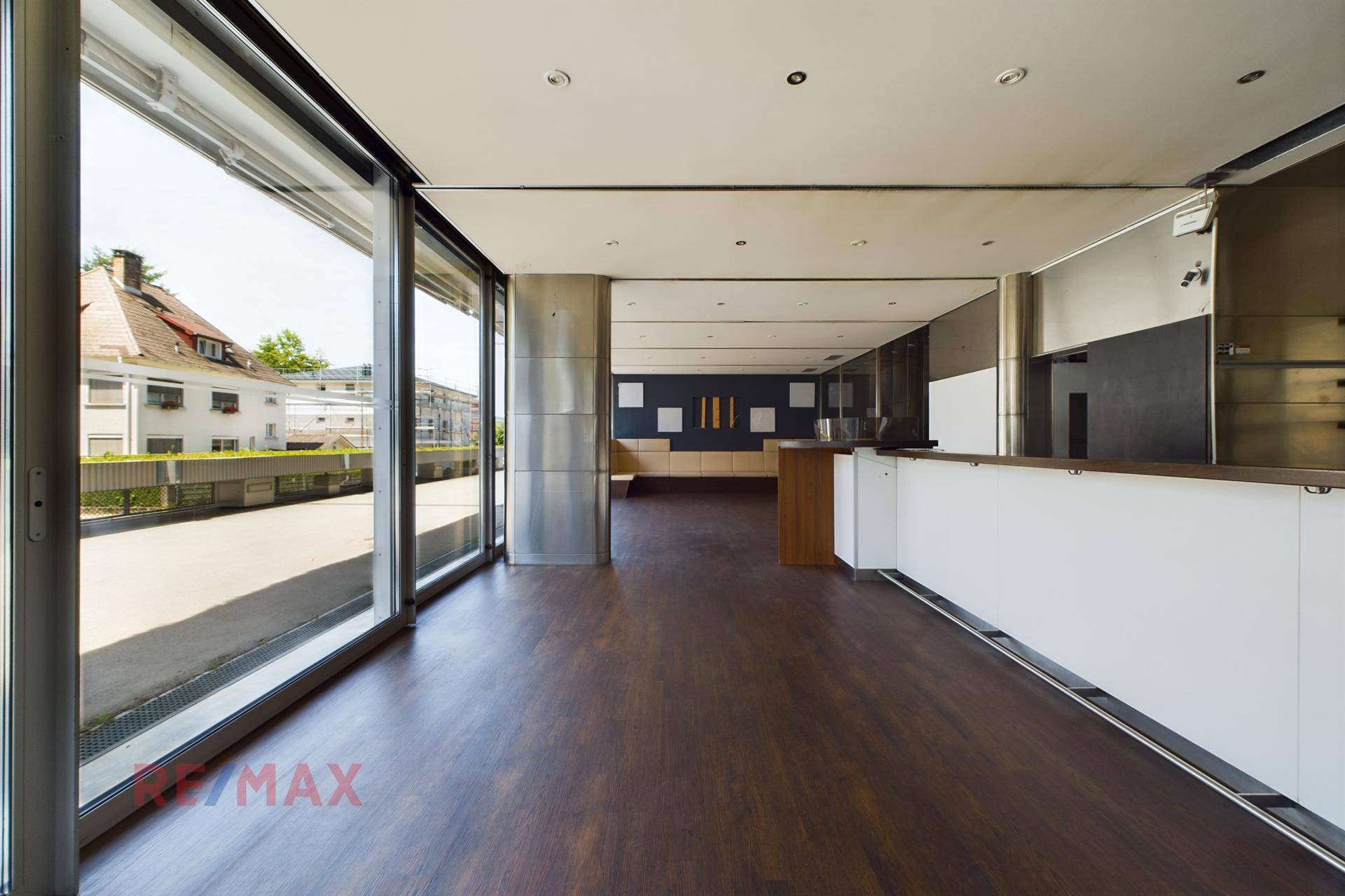 Geräumiger, offener Verkaufsraum mit großen Fensterfronten, dunklem Holzboden und moderner Ausstattung.