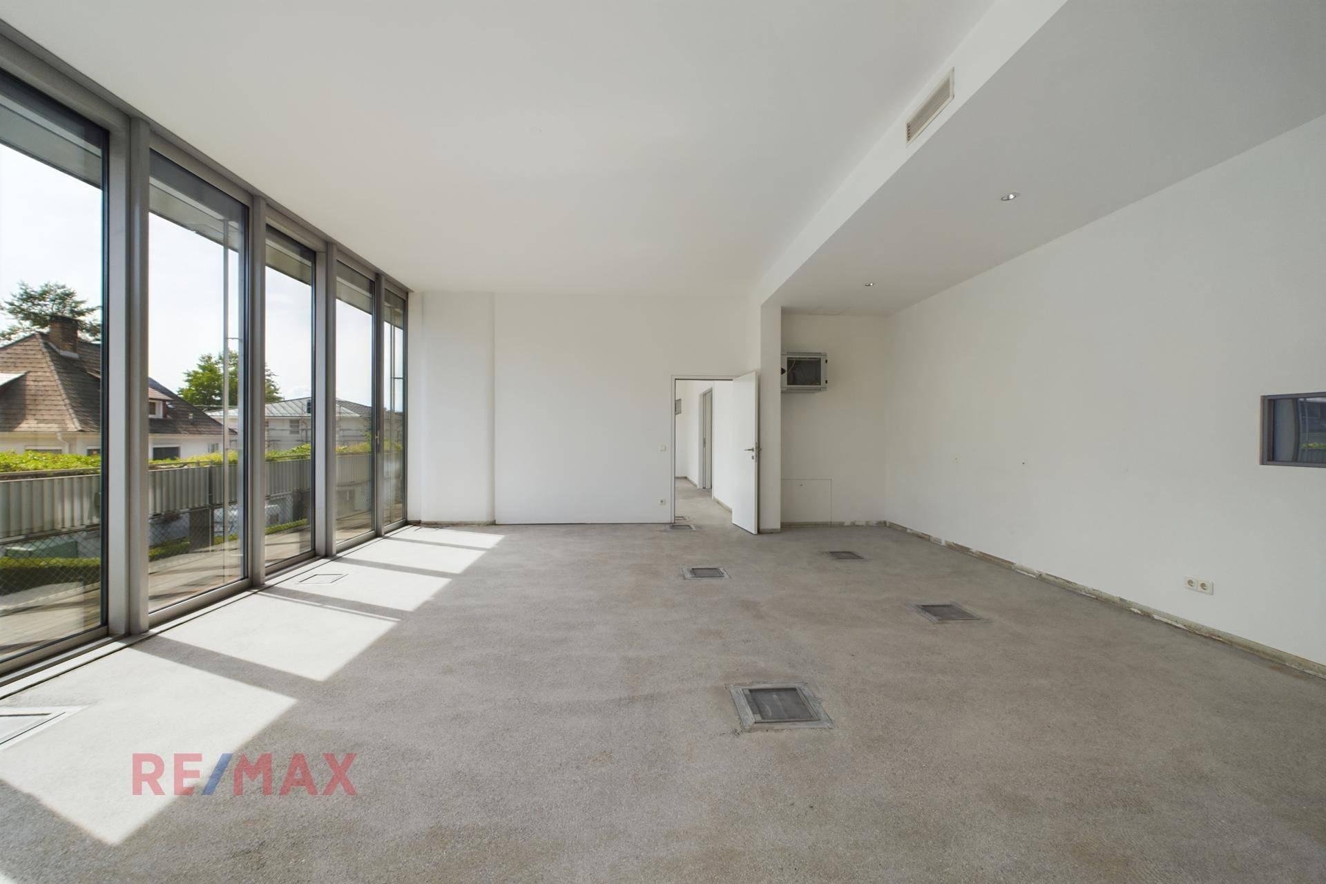 Offener Büroraum mit großen Fensterfronten, viel Tageslicht und Zugang zu weiteren Räumen.
