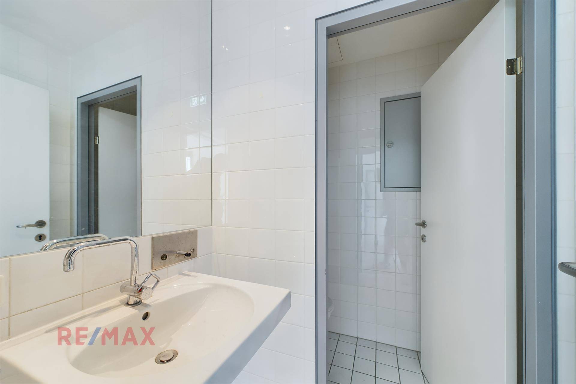 Modernes Badezimmer mit weiß gefliesten Wänden, Waschbecken, Spiegel und Duschbereich.