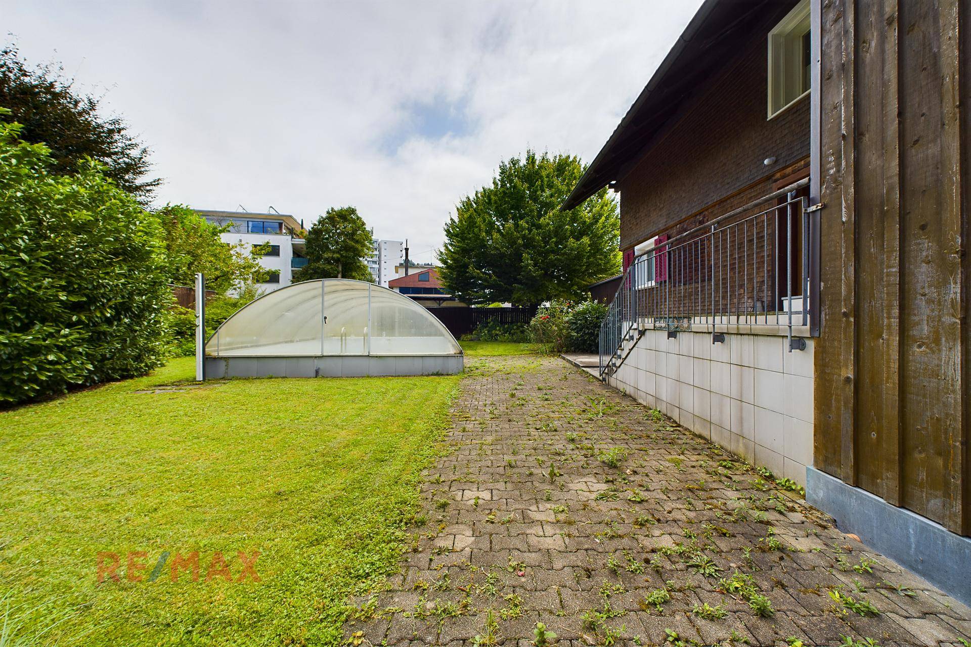 Seitenansicht des Hauses mit großem Garten, Rasenfläche, Gewächshaus und Zugang zur Terrasse.
