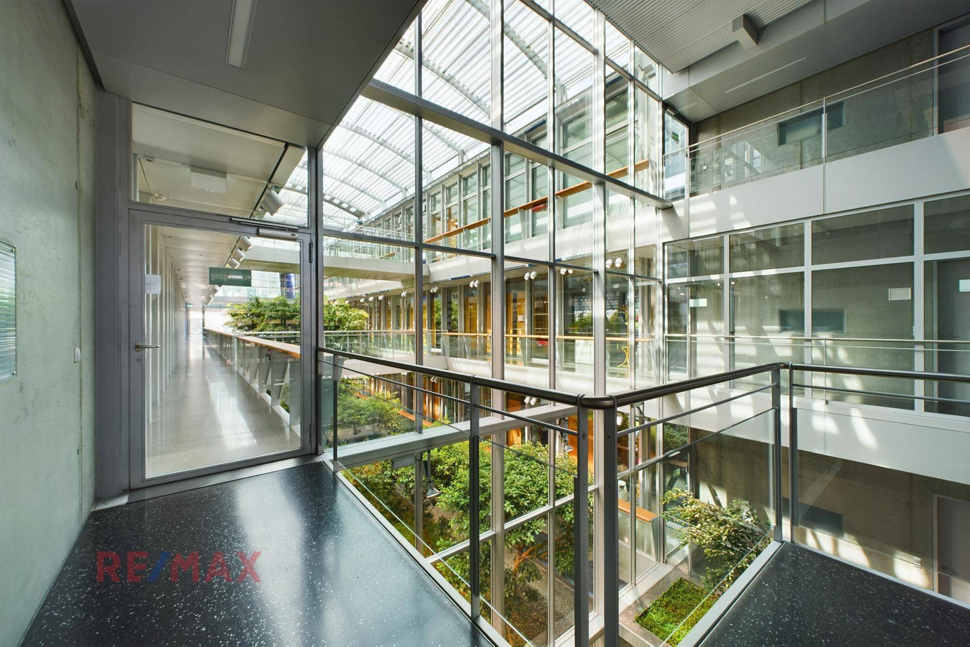 Helles Atrium mit Glasdach, mehreren Etagen und viel Grünpflanzen im Innenbereich des Gebäudes.