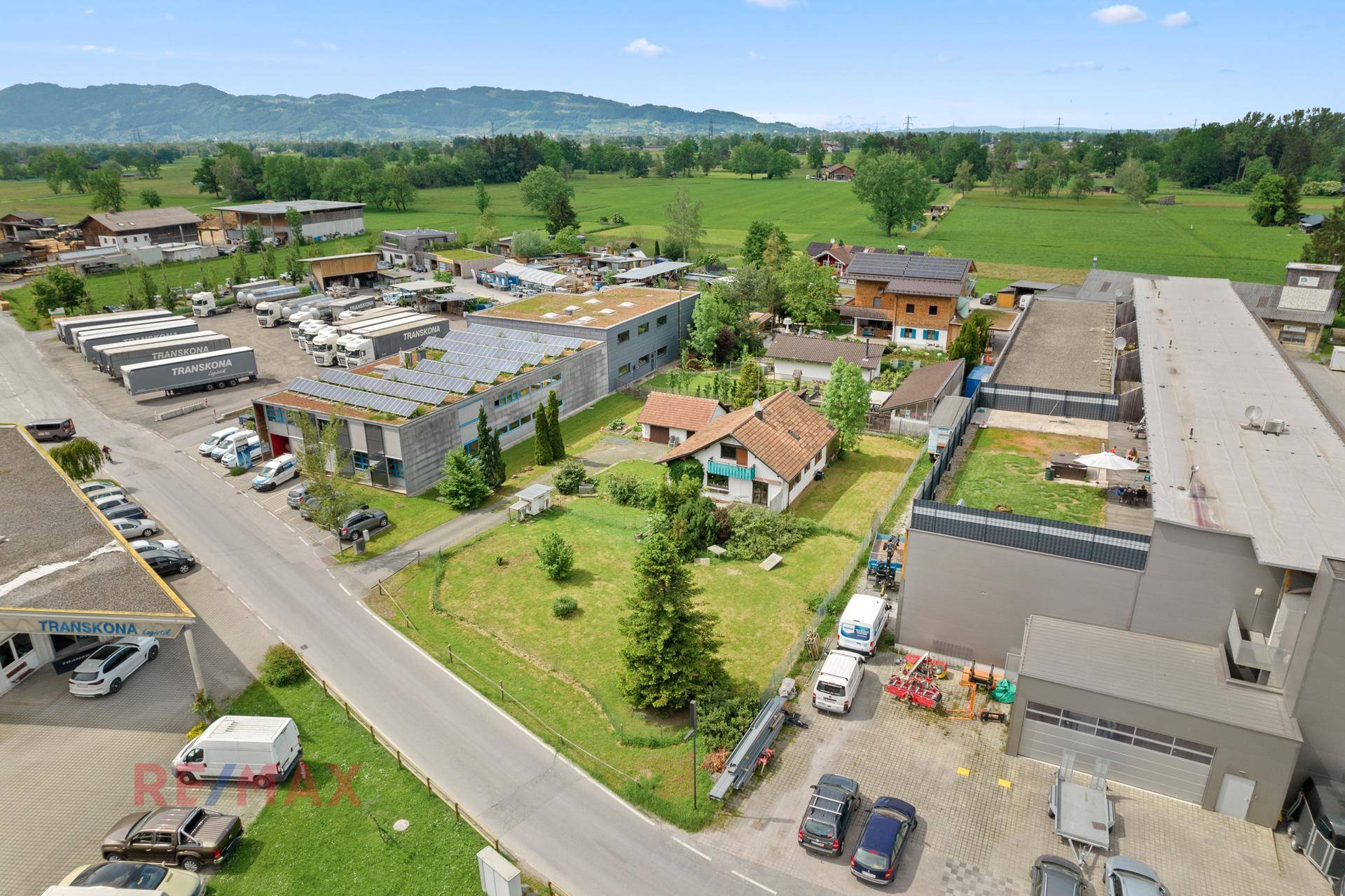 Weitläufige Ansicht des Anwesens mit umliegenden Gewerbeflächen, grünen Feldern und einer Straße.