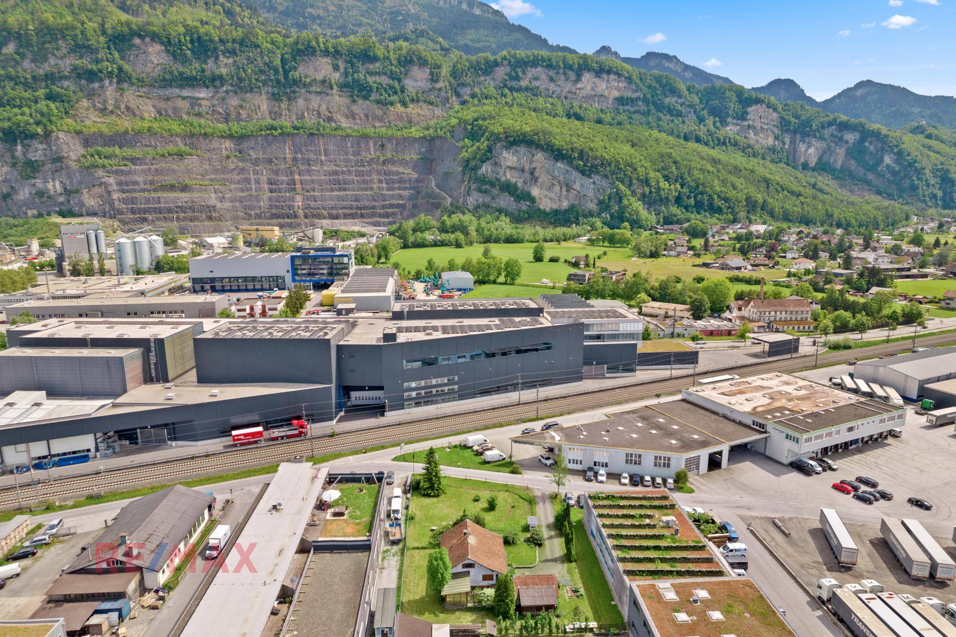 Luftaufnahme des Grundstücks mit Industriegebiet, Bahngleisen und beeindruckender Bergkulisse im Hintergrund.