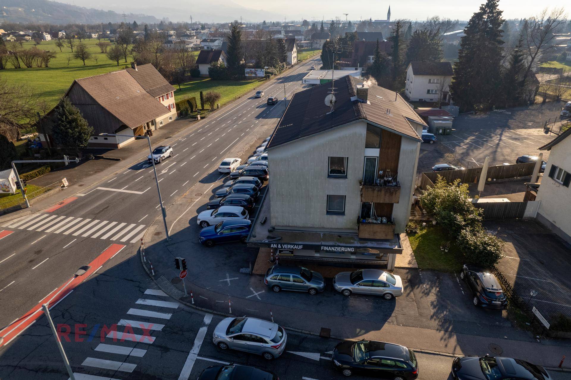 Nahaufnahme des Gebäudes mit Balkonen und der belebten Straße im Vordergrund, umgeben von Parkplätzen.