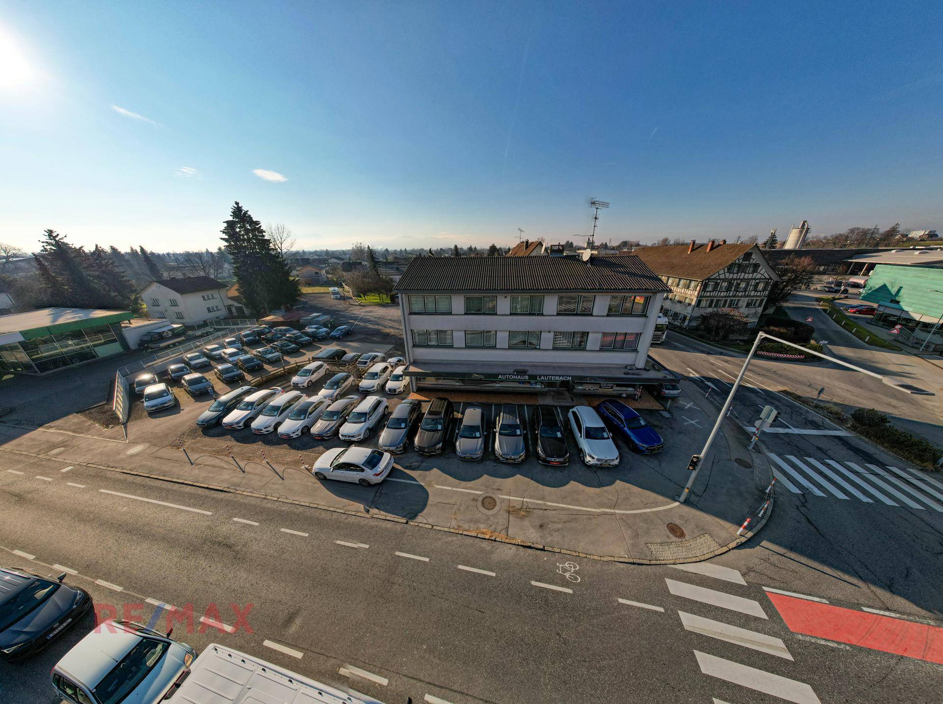 Weitwinkel-Luftaufnahme des Autohauses mit großem Parkplatz unter strahlendem Sonnenschein.