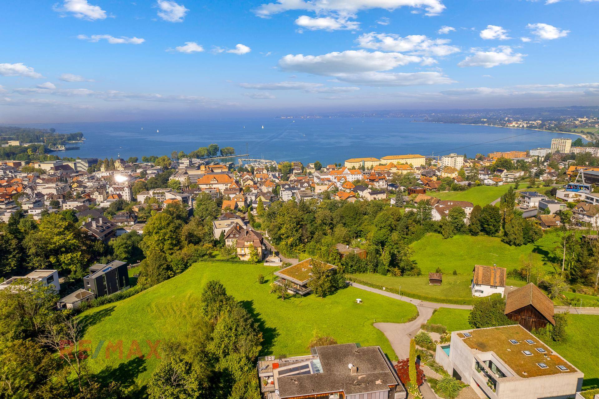 Weitläufiger Blick über eine Stadt und den angrenzenden See unter strahlend blauem Himmel.