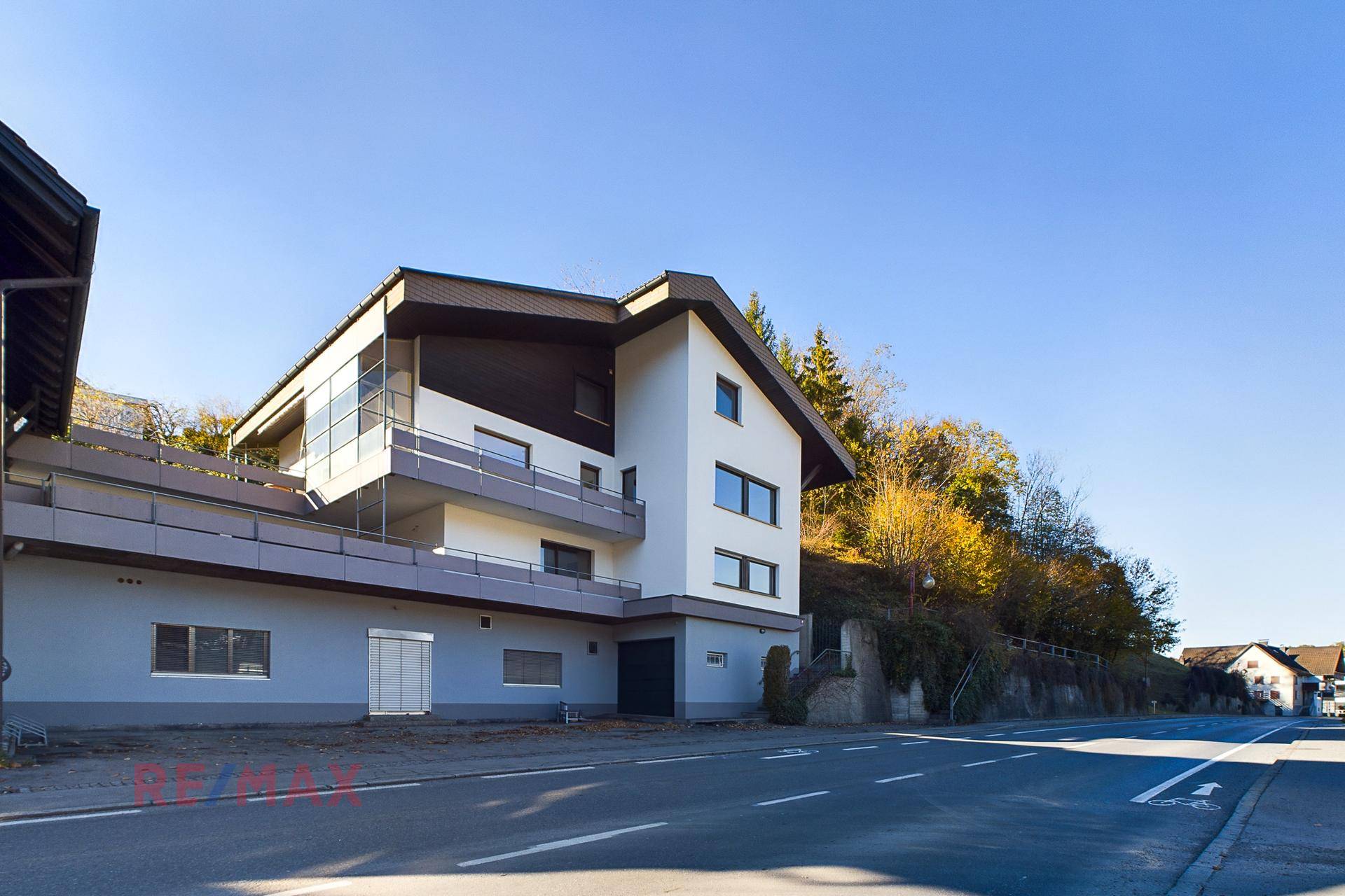 Ansicht des Gebäudes mit weißer Fassade und Balkonen unter blauem Himmel und grüner Umgebung.
